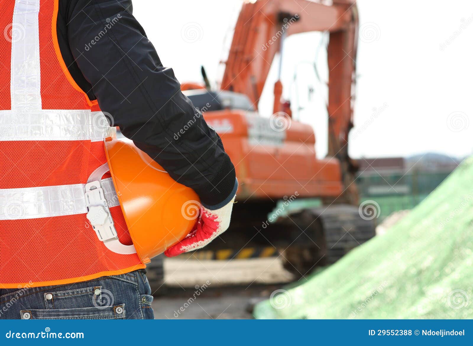 Trabajador del concepto de la seguridad de construcción que sostiene el casco de protección con el excavador en el fondo