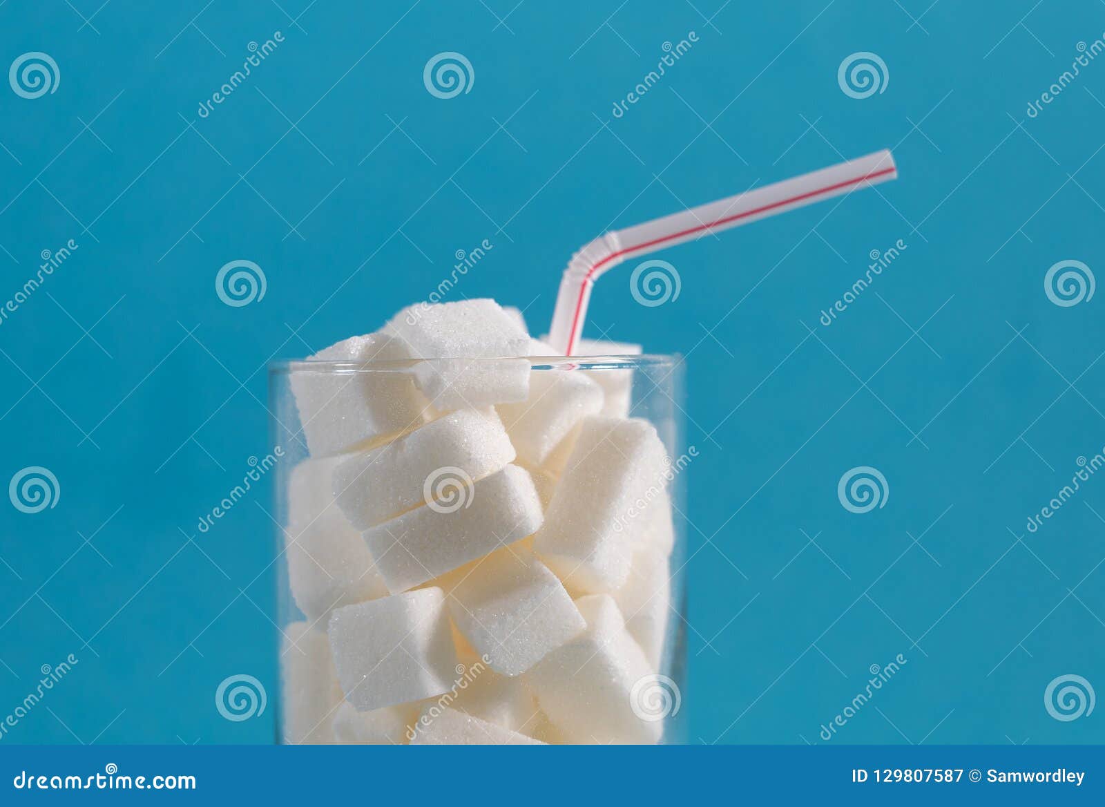 conceptual still life image of glass full of sugar cubes and straw in excess of calories in soft drinks