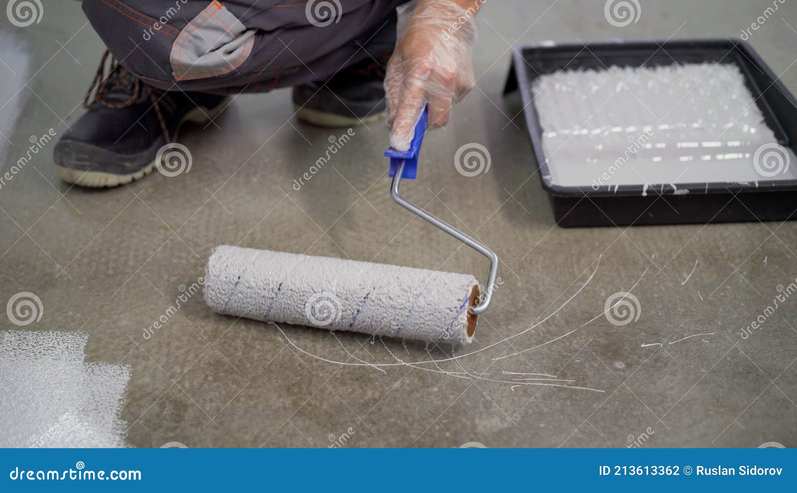 A Worker Paints the Concrete Floor with a Roller White. Concrete Floor