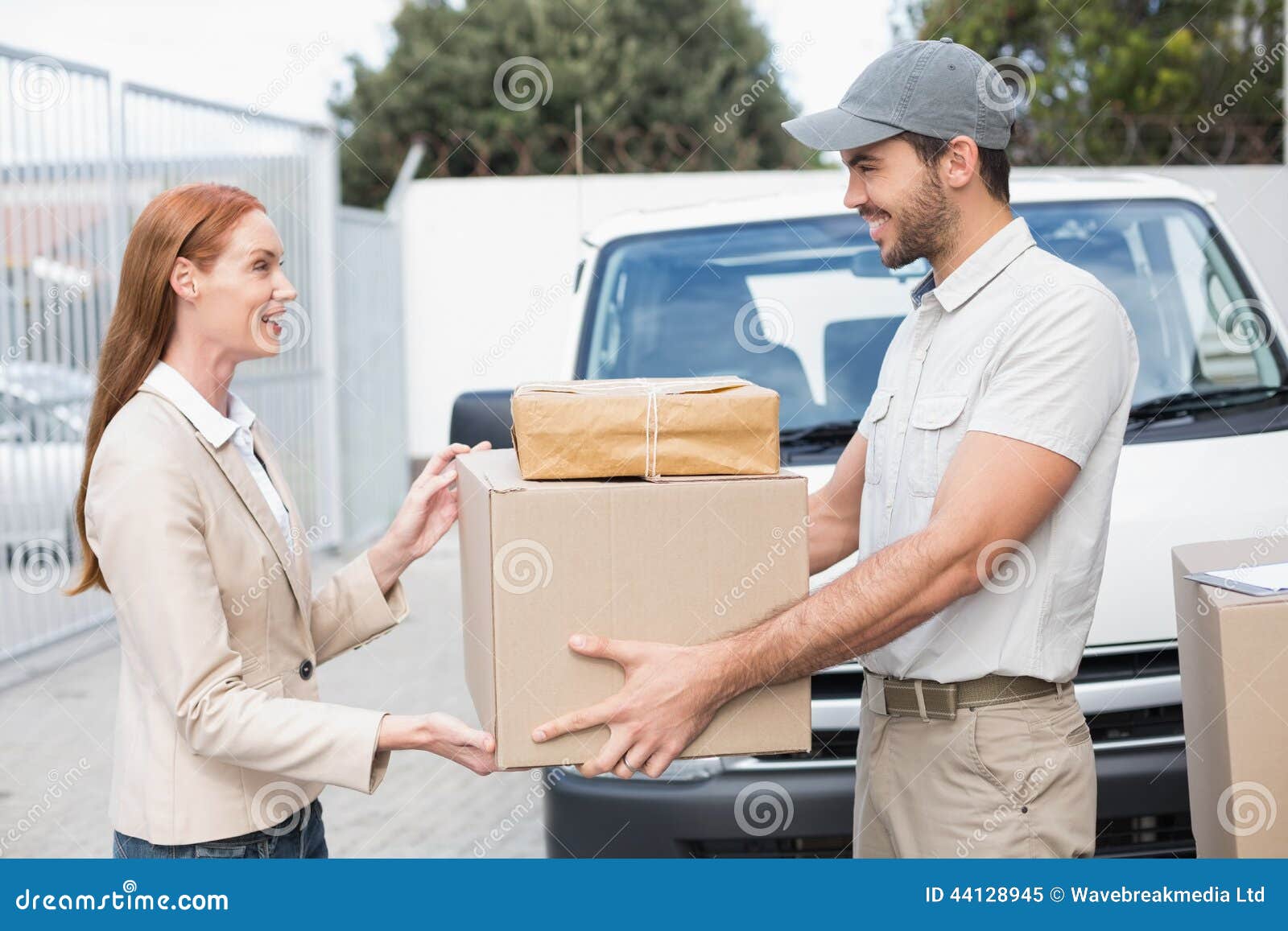 Conductor de la entrega que pasa paquetes al cliente feliz fuera del almacén