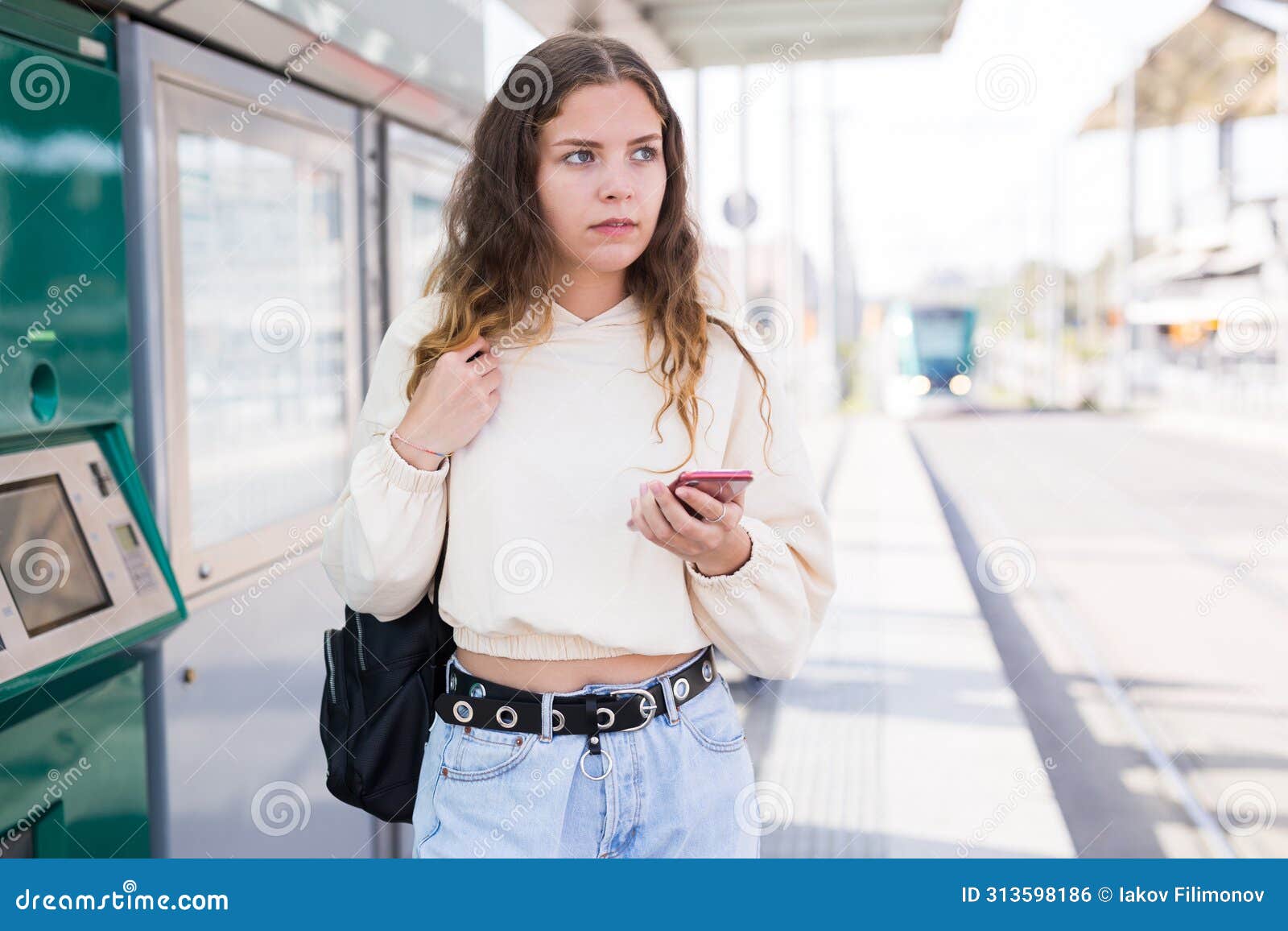confident girl walking along a tram stop holds a mobile phone
