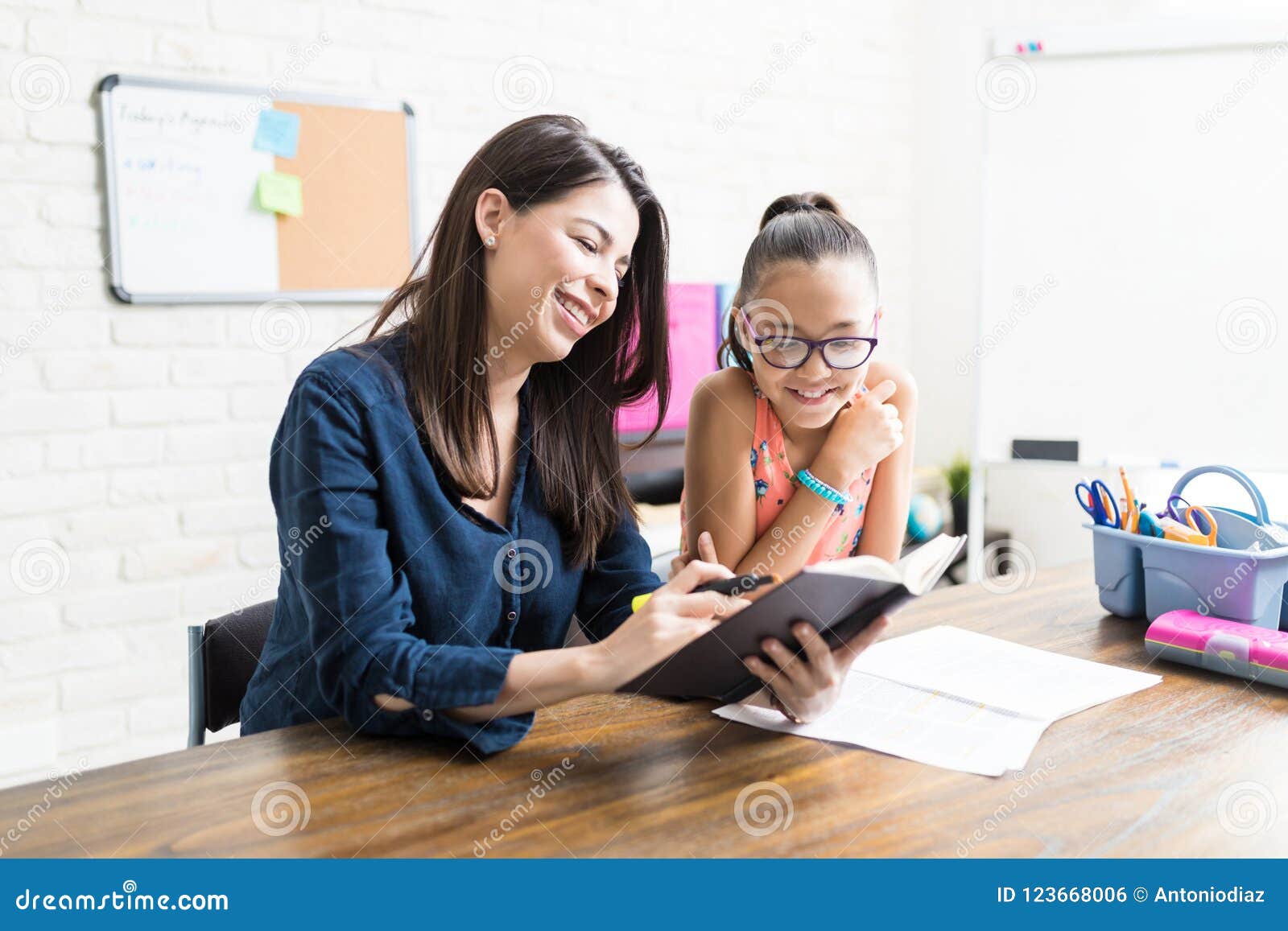 confident mother reading book to girl at table