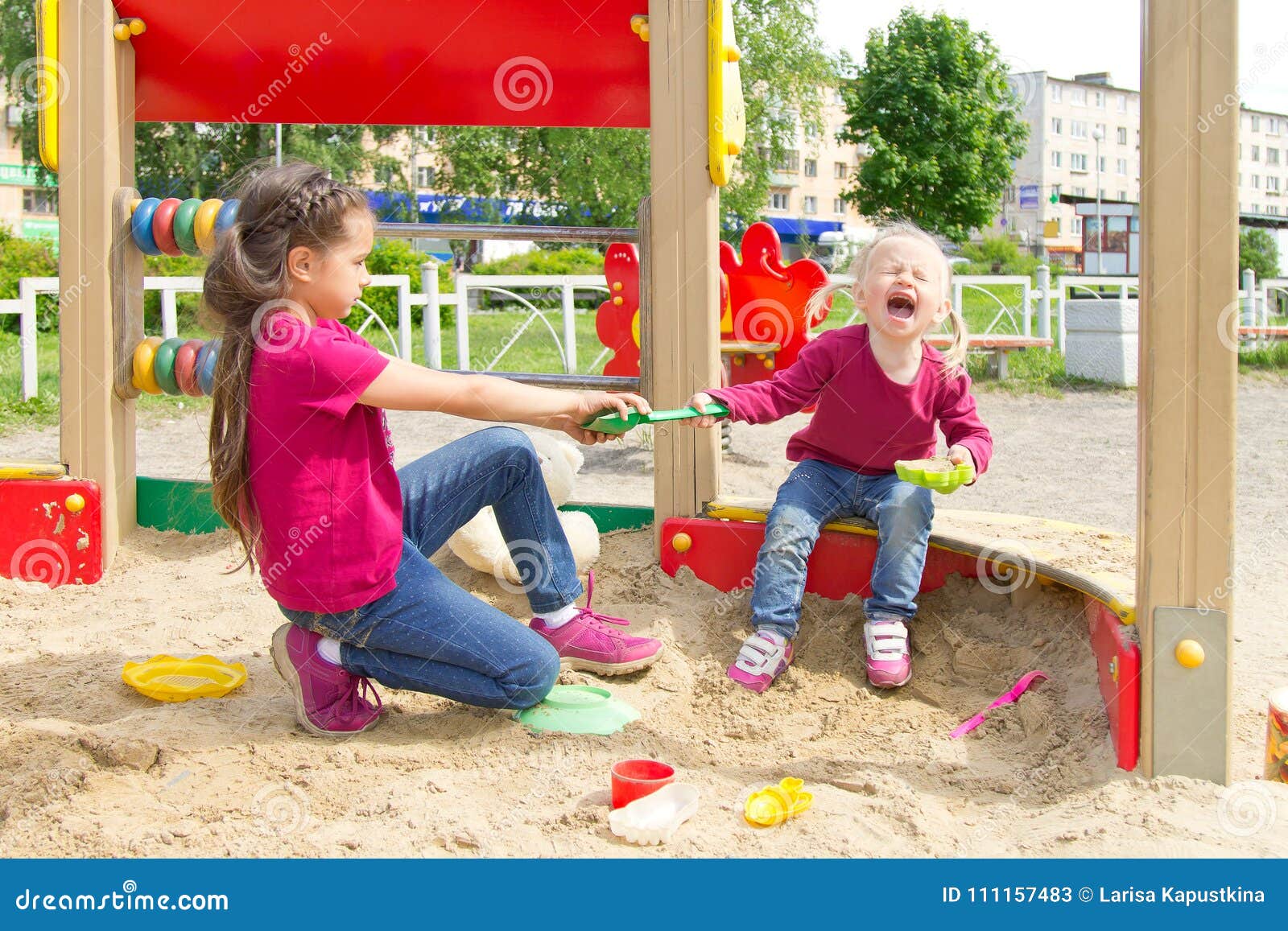 conflict on the playground. two sisters fighting over a toy shovel in the sandbox