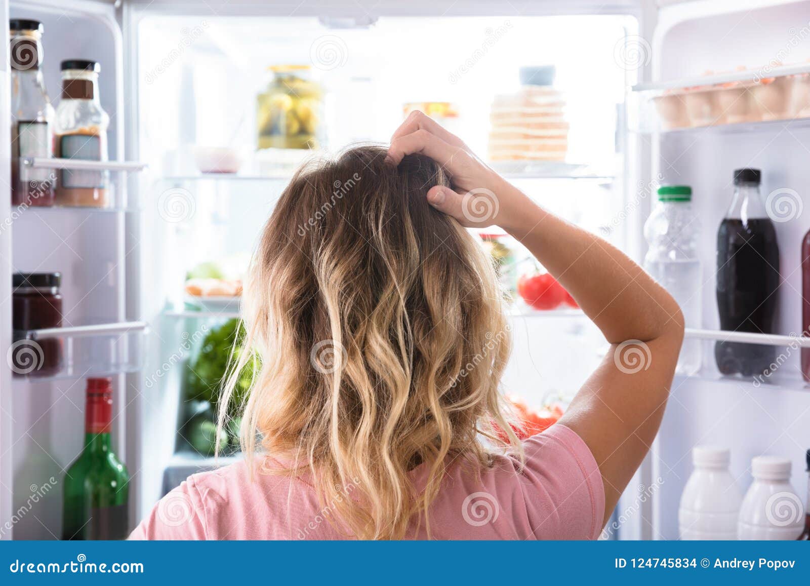 confused woman looking in open refrigerator
