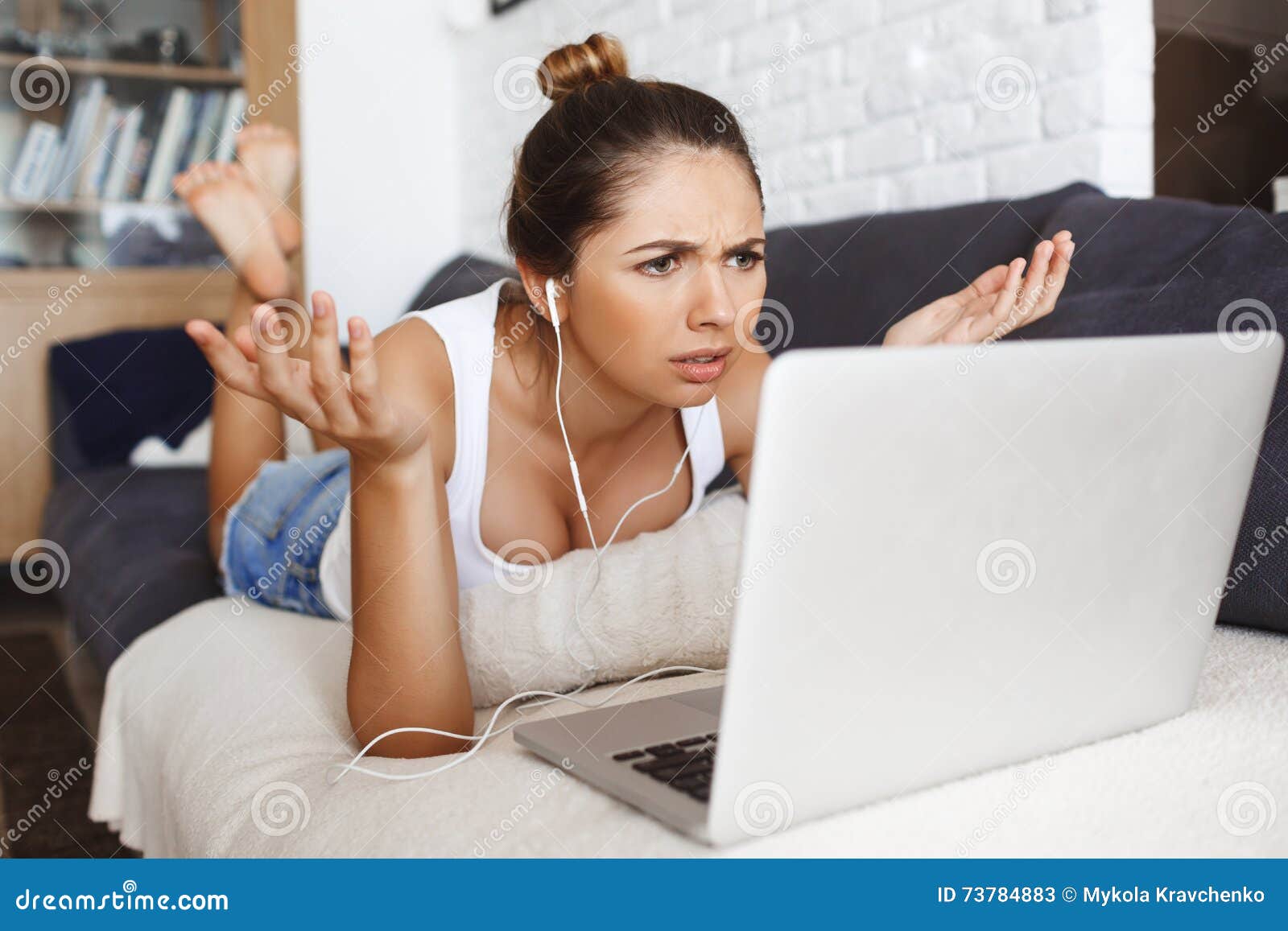 Confused Young Girl Lying On Sofa At Living Room With Laptop Stock