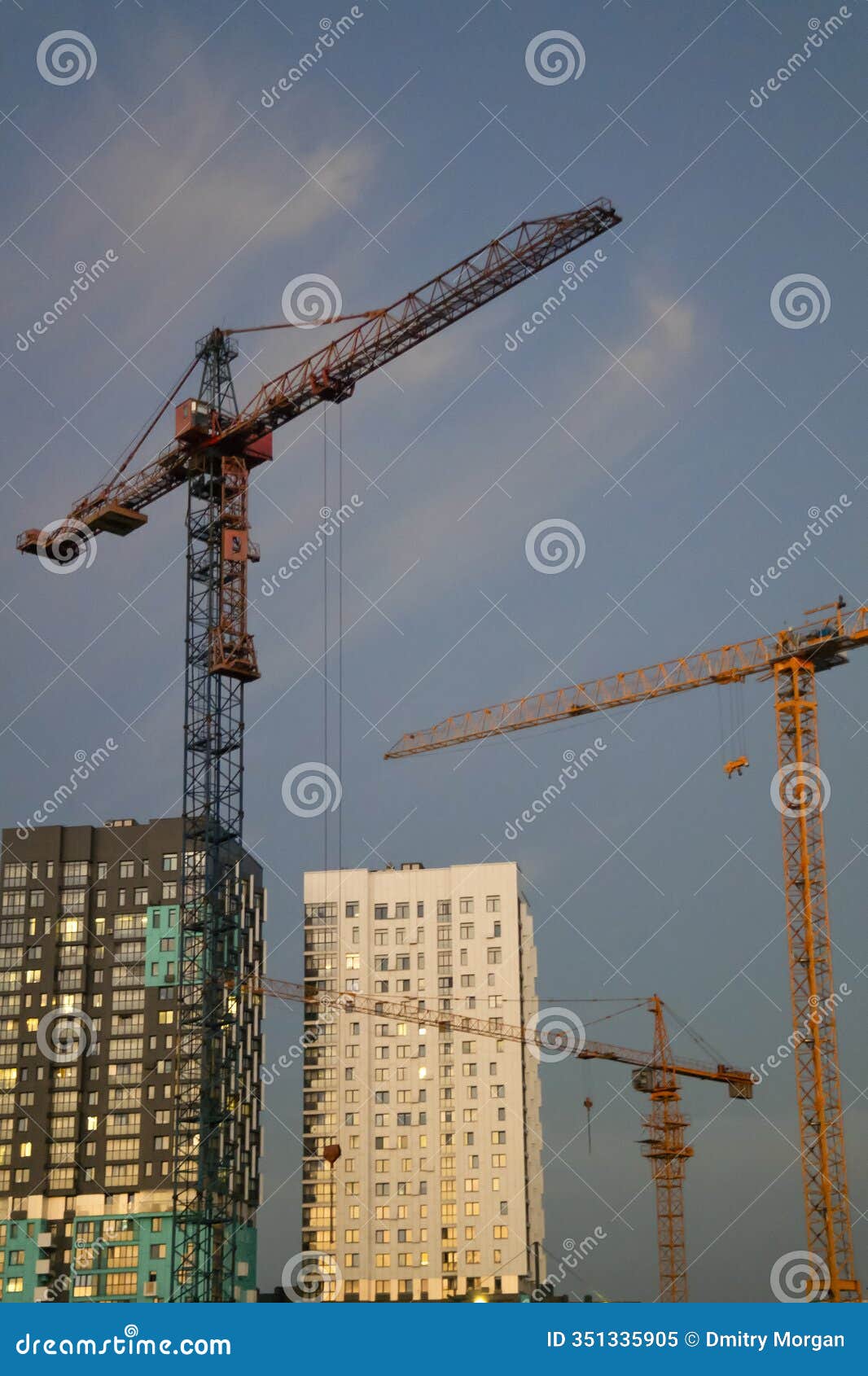 construction ideas. variety of tower construction cranes on building site against blue evening sky background
