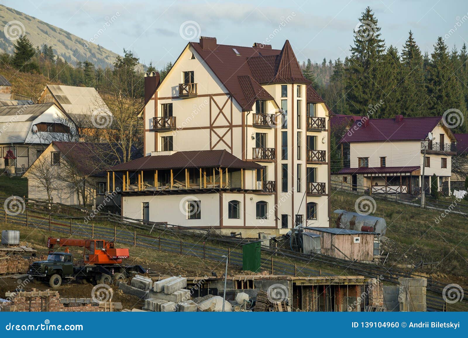 construction site with building crane and new modern comfortable hotel house with shingled roof in ecological rural area on spruce