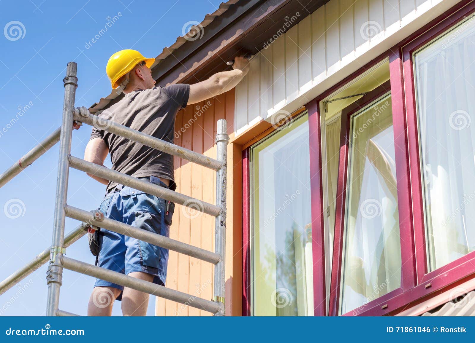 construction worker on scaffolding painting wooden house facade