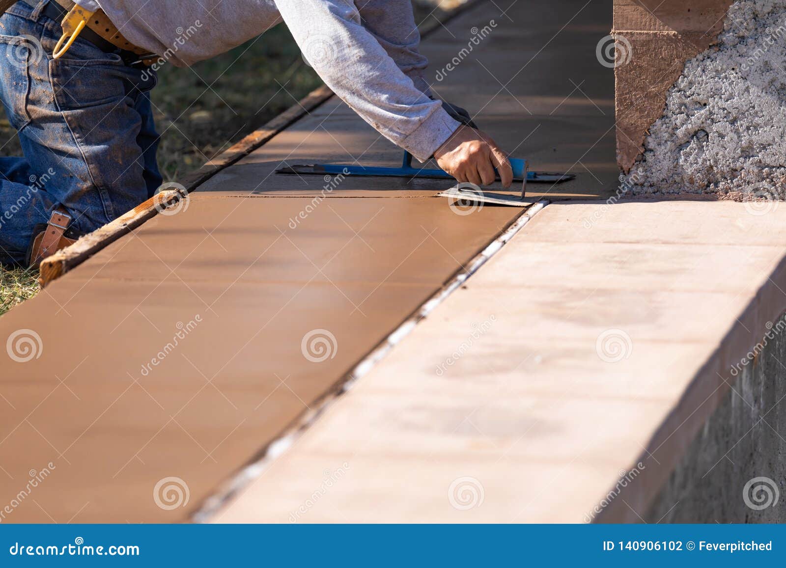 construction worker smoothing wet cement with hand edger tool