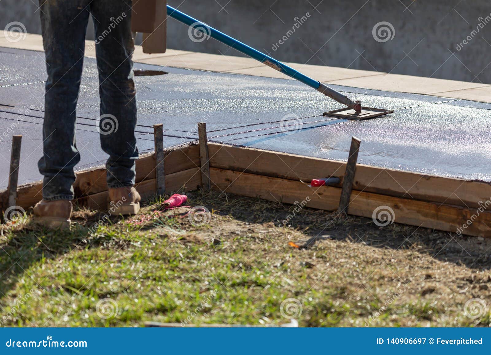 construction worker smoothing wet cement with long handled edger tool