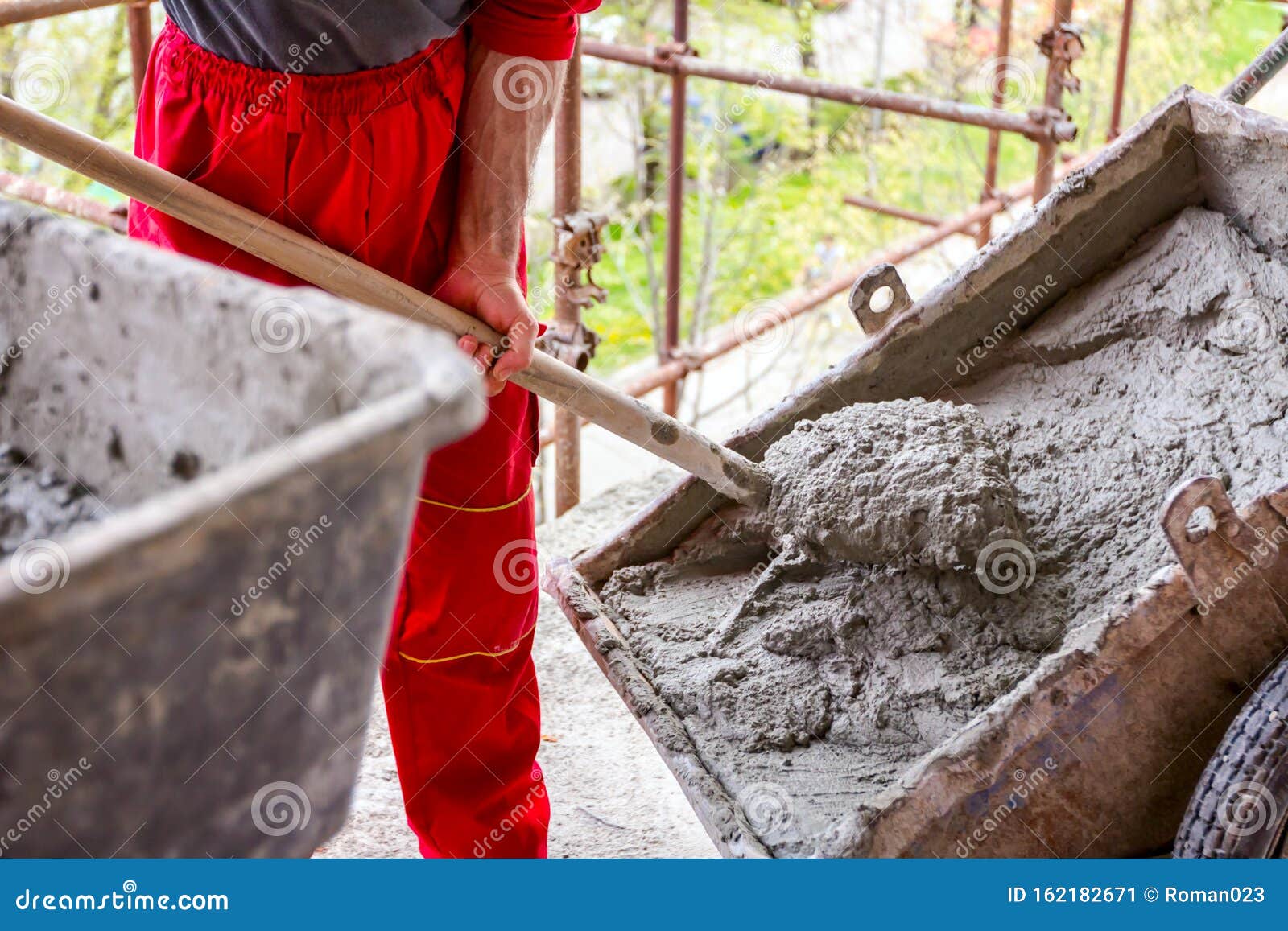 Worker is Using Shovel To Unload Wheelbarrow at Building Site Stock