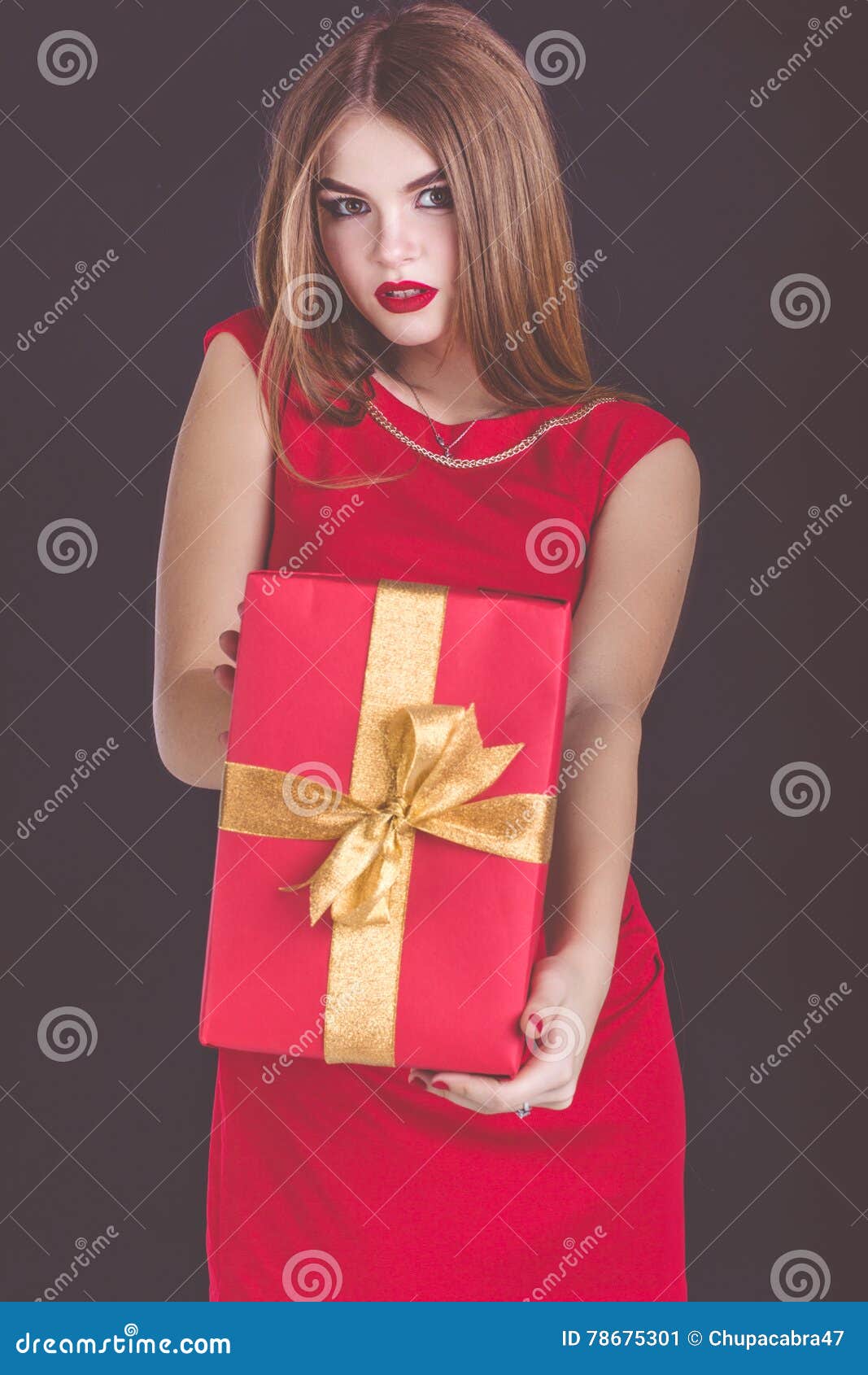 Contenitore di regalo rosso di bello della ragazza natale della tenuta. La bella ragazza sorridente sta portando il vestito rosso da modo che giudica il contenitore di regalo rosso isolato sul nero, concetto di natale