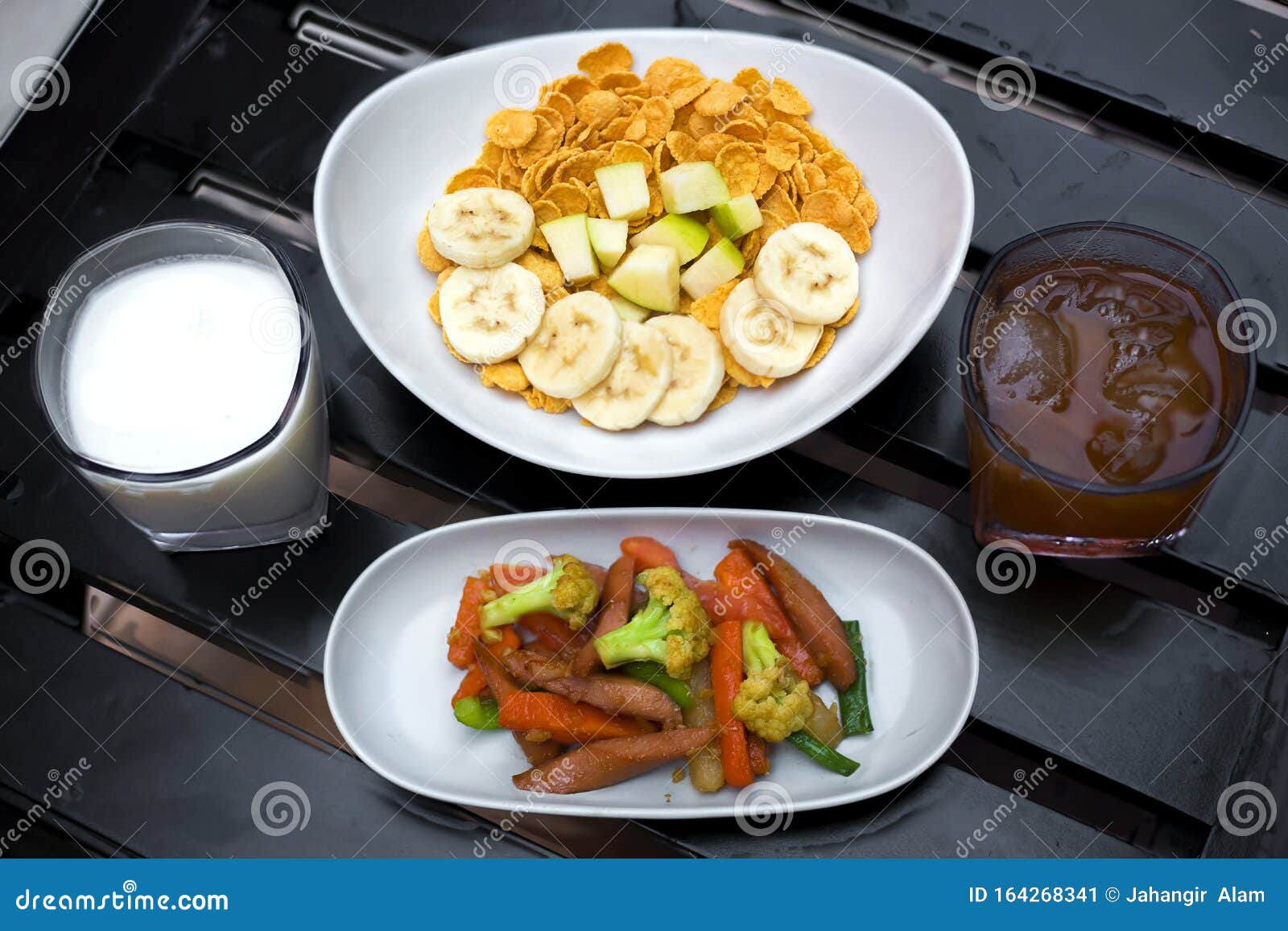 continental breakfast Ã¢â¬â cornflakes with fruits, milk and tea and some of saute vegetabls on black wood table. top view