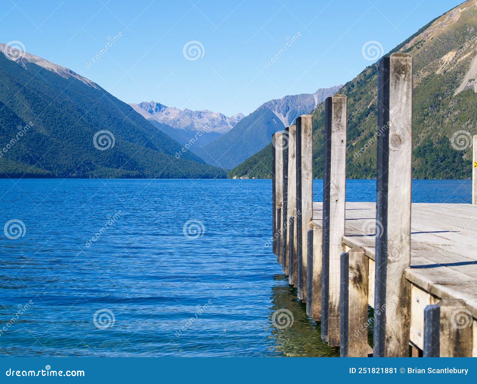 converging mountain ridges beyond stunning blue water and jetty on lake roto-iti