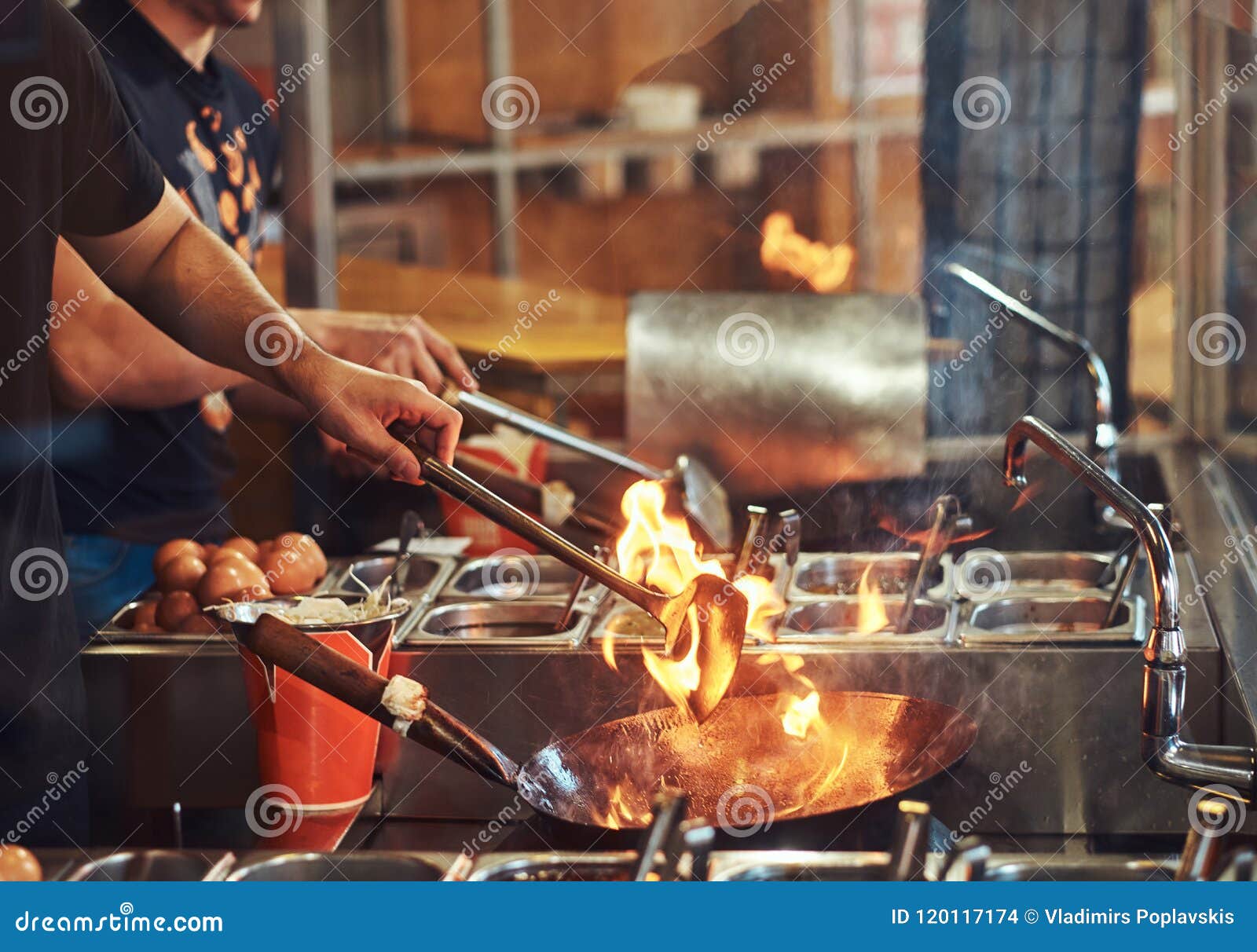 Unrecognizable man cooking in fatiscent big pan or wok in a small