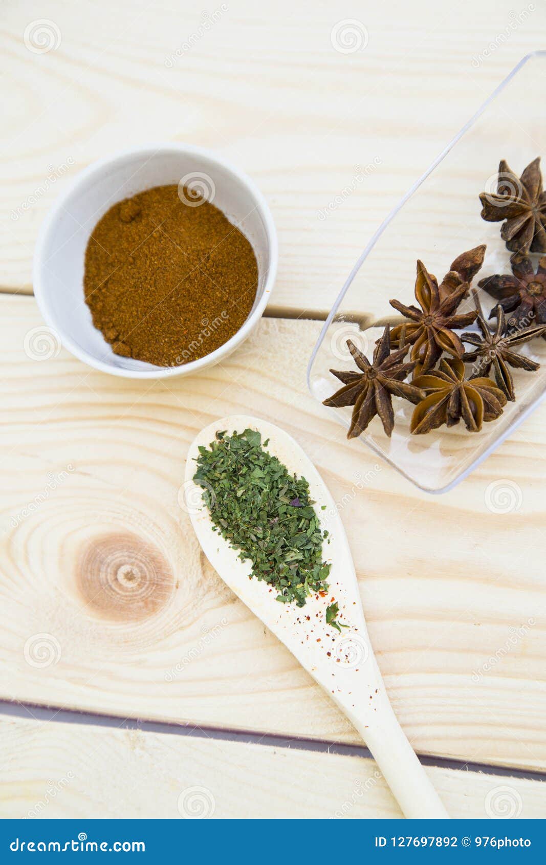 cooking hot spicy food concept. dry spices, beans and herbs in wooden and glass spoons and palstic cup on light wooden table