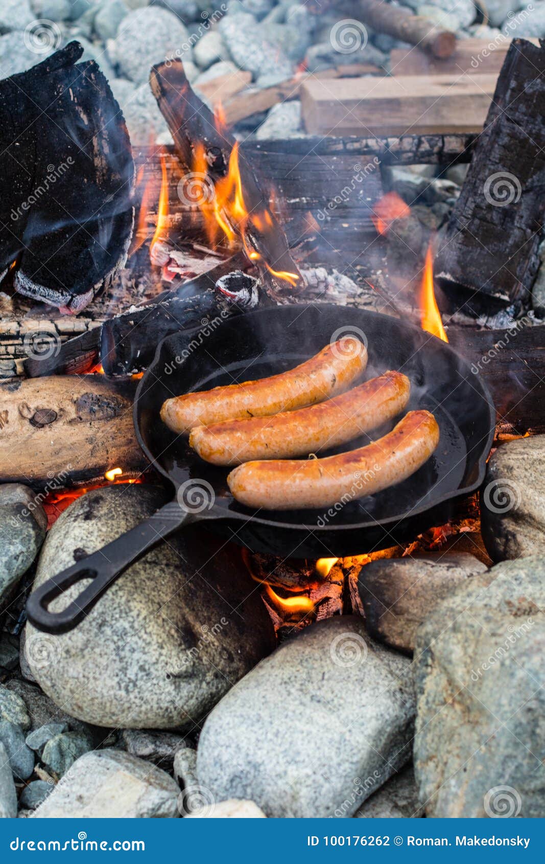 Cooking sausages in cast iron skillet on campfire while camping. Good and  positive campfire food. Stock Photo