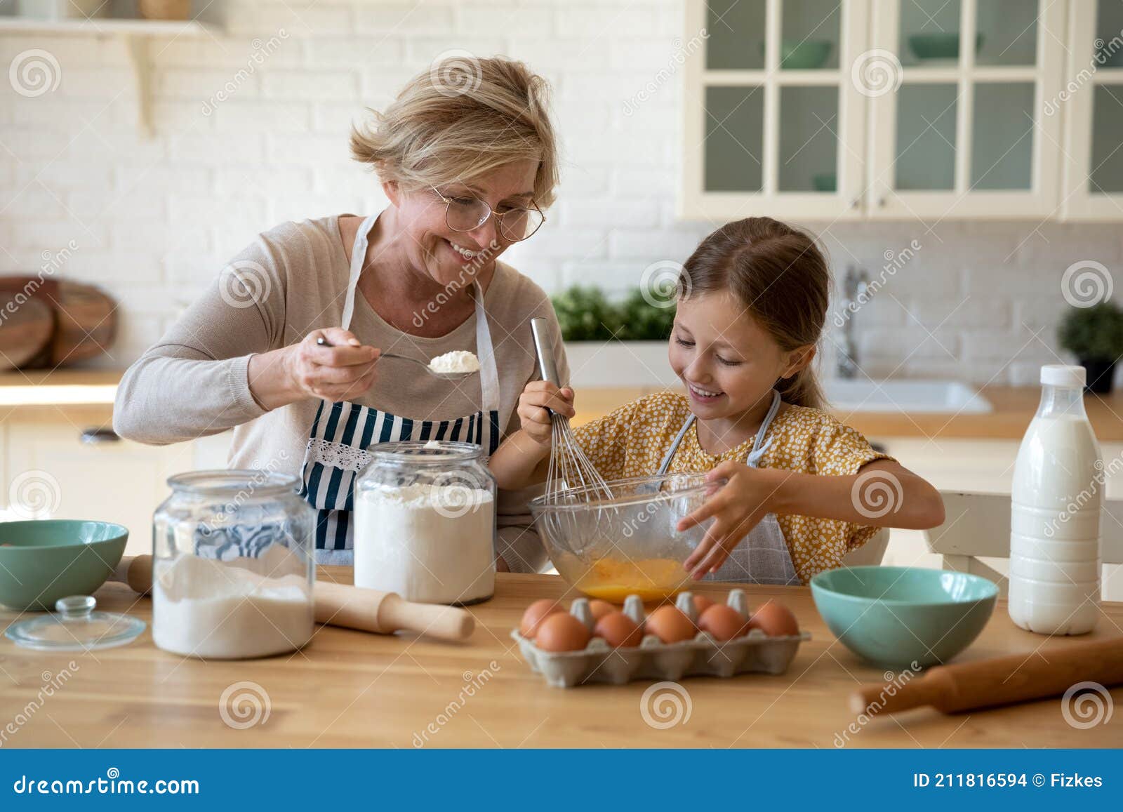 happy little girl help senior grandma at kitchen mix dough