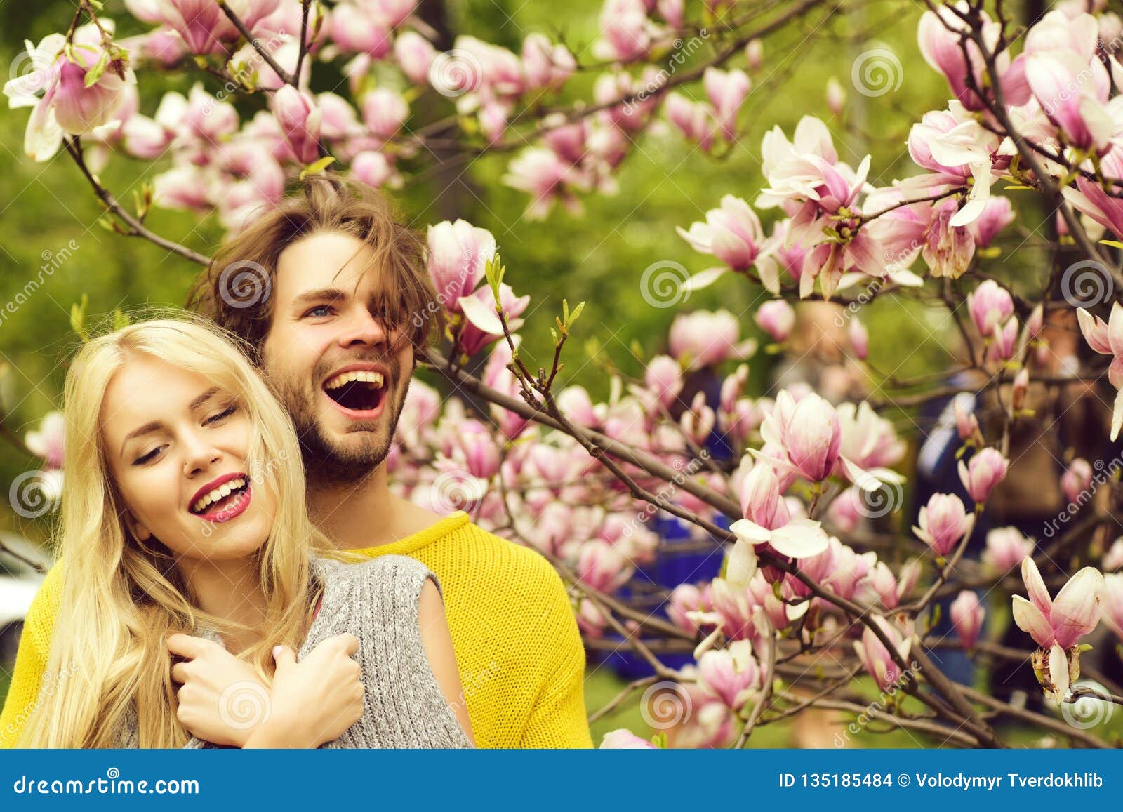 Coppie felici nell'amore nei fiori della magnolia di primavera. Sorgente la coppia felice nell'amore nella magnolia di primavera fiorisce, uomini e ragazza sorridenti in giardino con l'albero del fiore all'aperto su sfondo naturale