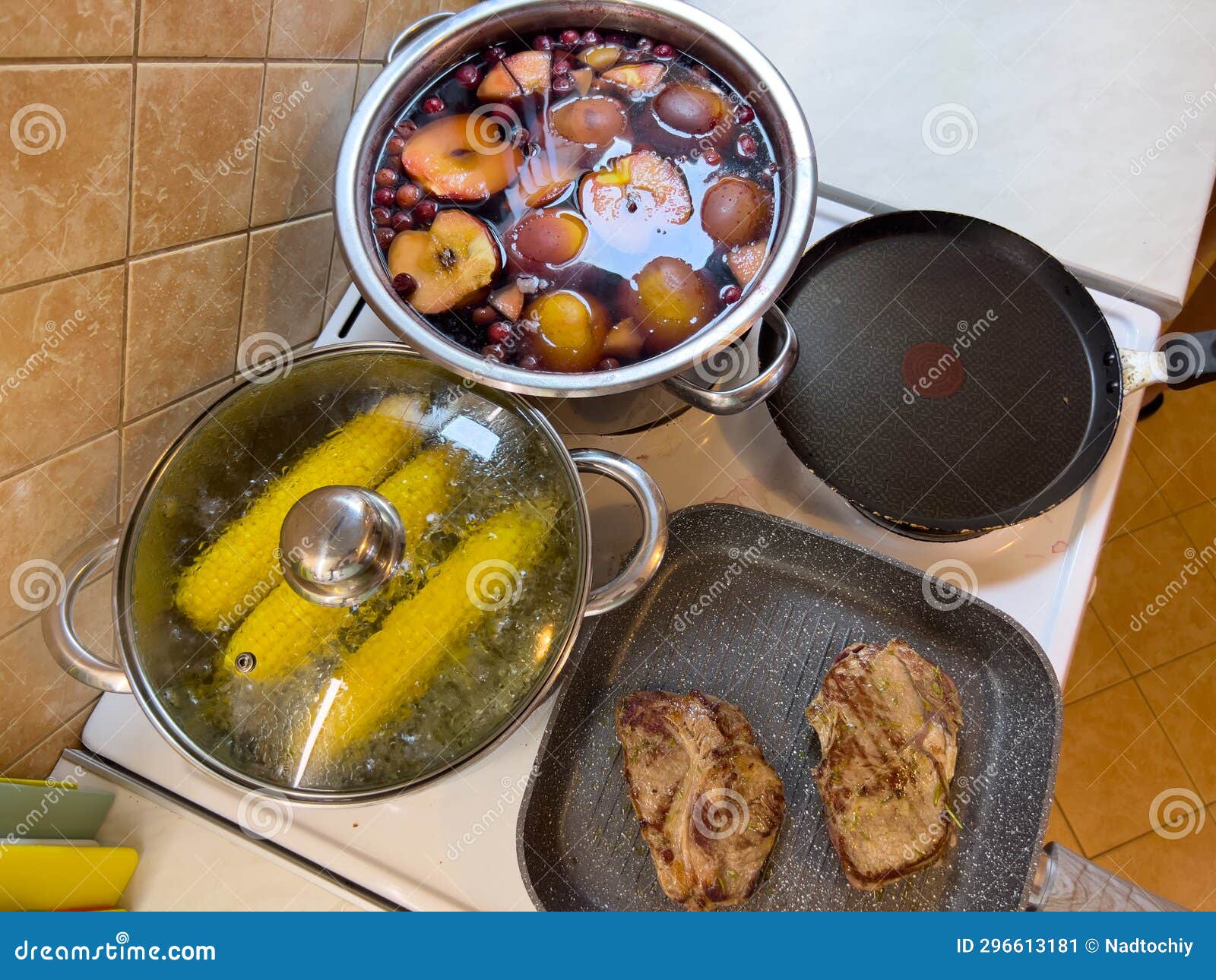 Corn Cobs are Boiled in a Saucepan Next To Compote and Steaks Fried in