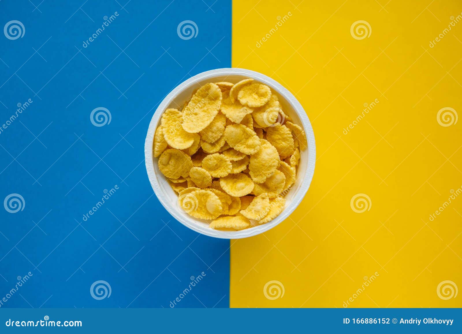 Cornflakes in White Bowl on Blue and Yellow Background. Top View Stock