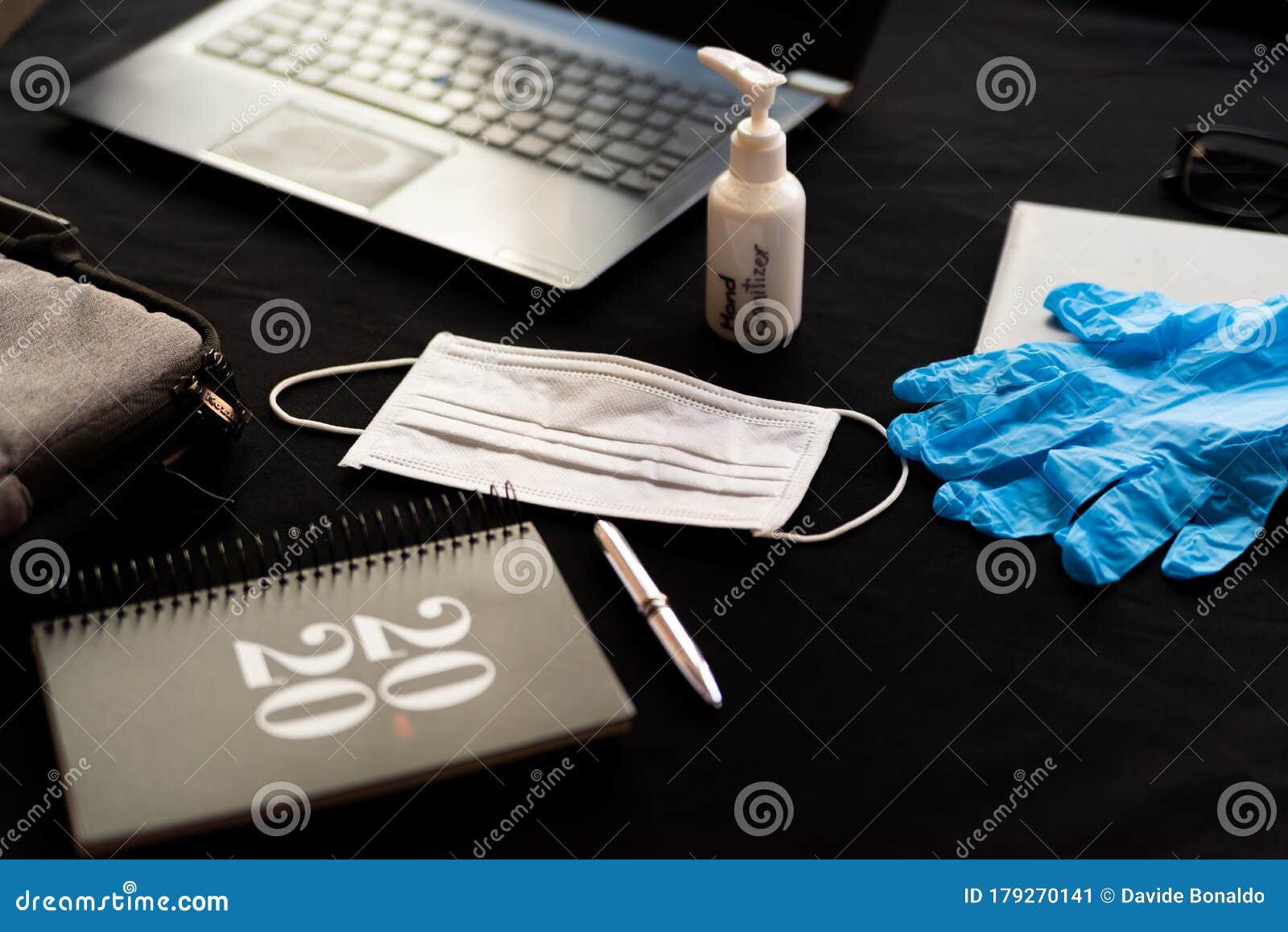 coronavirus remote work kit on wooden office desk with hand sanitizer and face mask and 2020 agenda, against the spread of corona