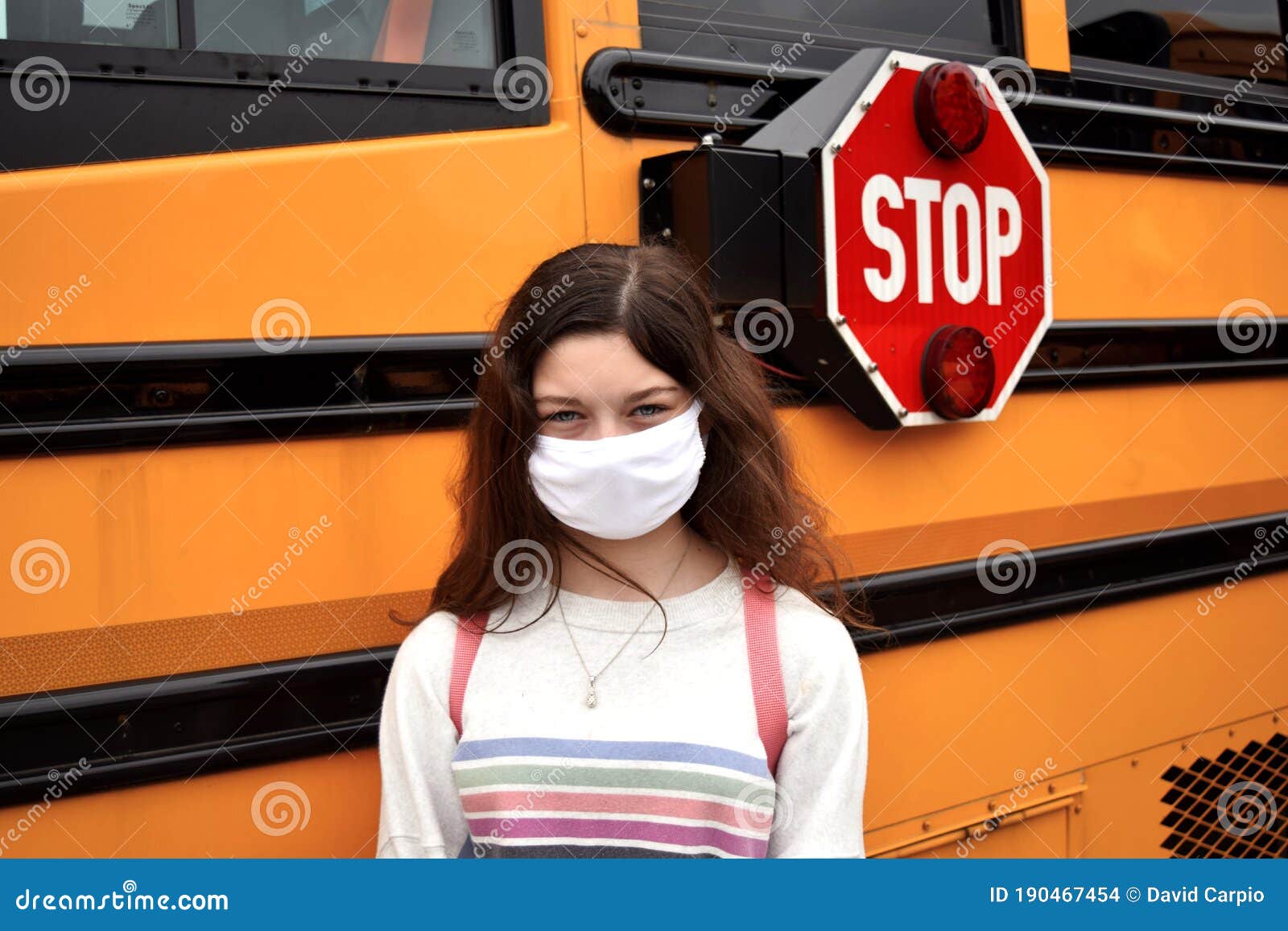 coronavirus school reopening concept: girl with face mask by school bus