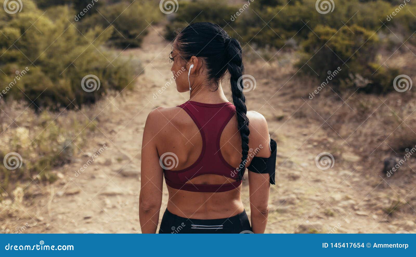 Corredor antes de un funcionamiento del campo a través. Vista posterior de la situación joven de la mujer de los deportes en el camino de tierra y de la mirada lejos Corredor femenino antes de un funcionamiento en la trayectoria del campo a través