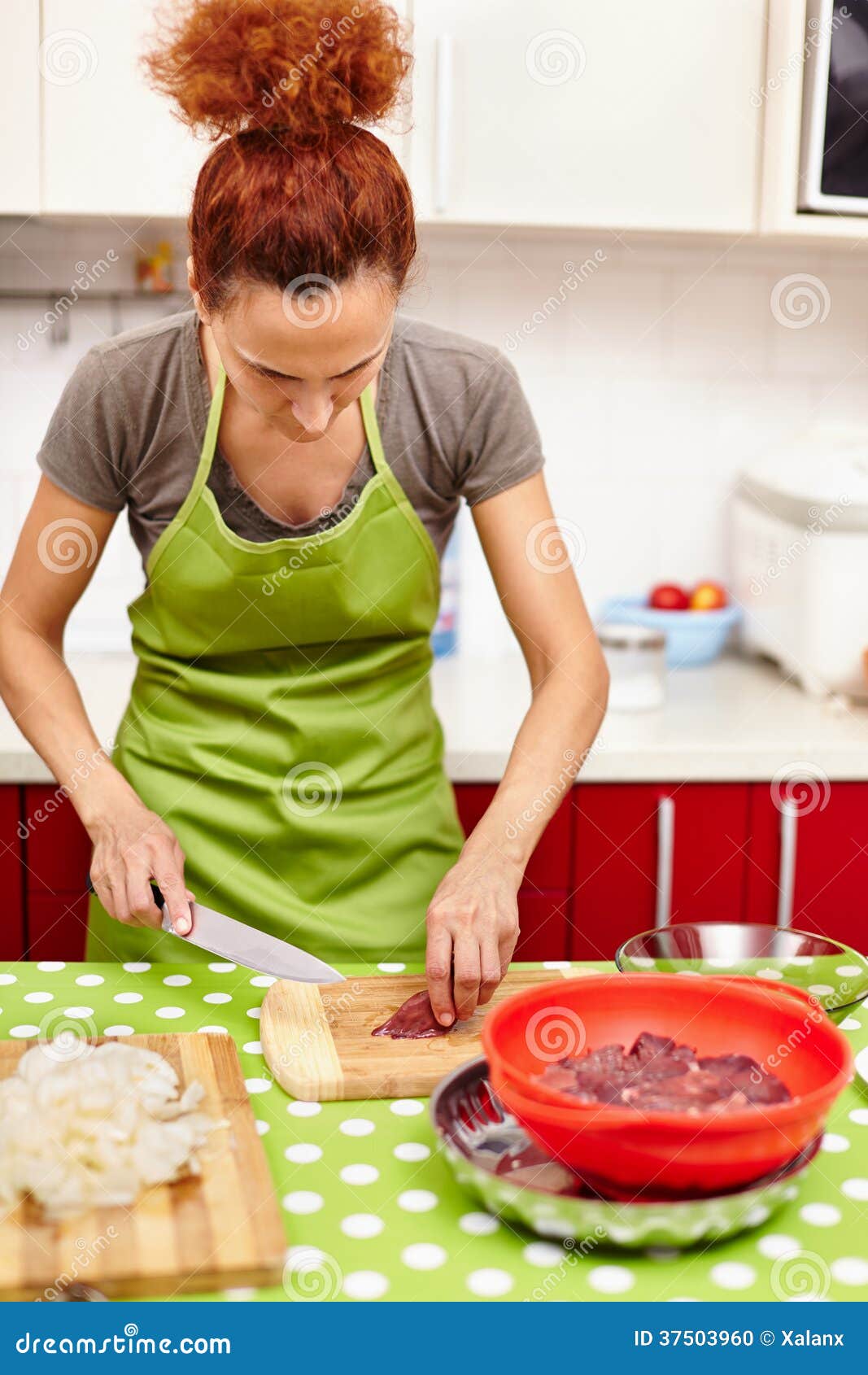 Cortar el hígado de pollo para la cena. Mujer caucásica que corta el hígado de pollo en un tablero de madera, al lado de la cebolla cortada