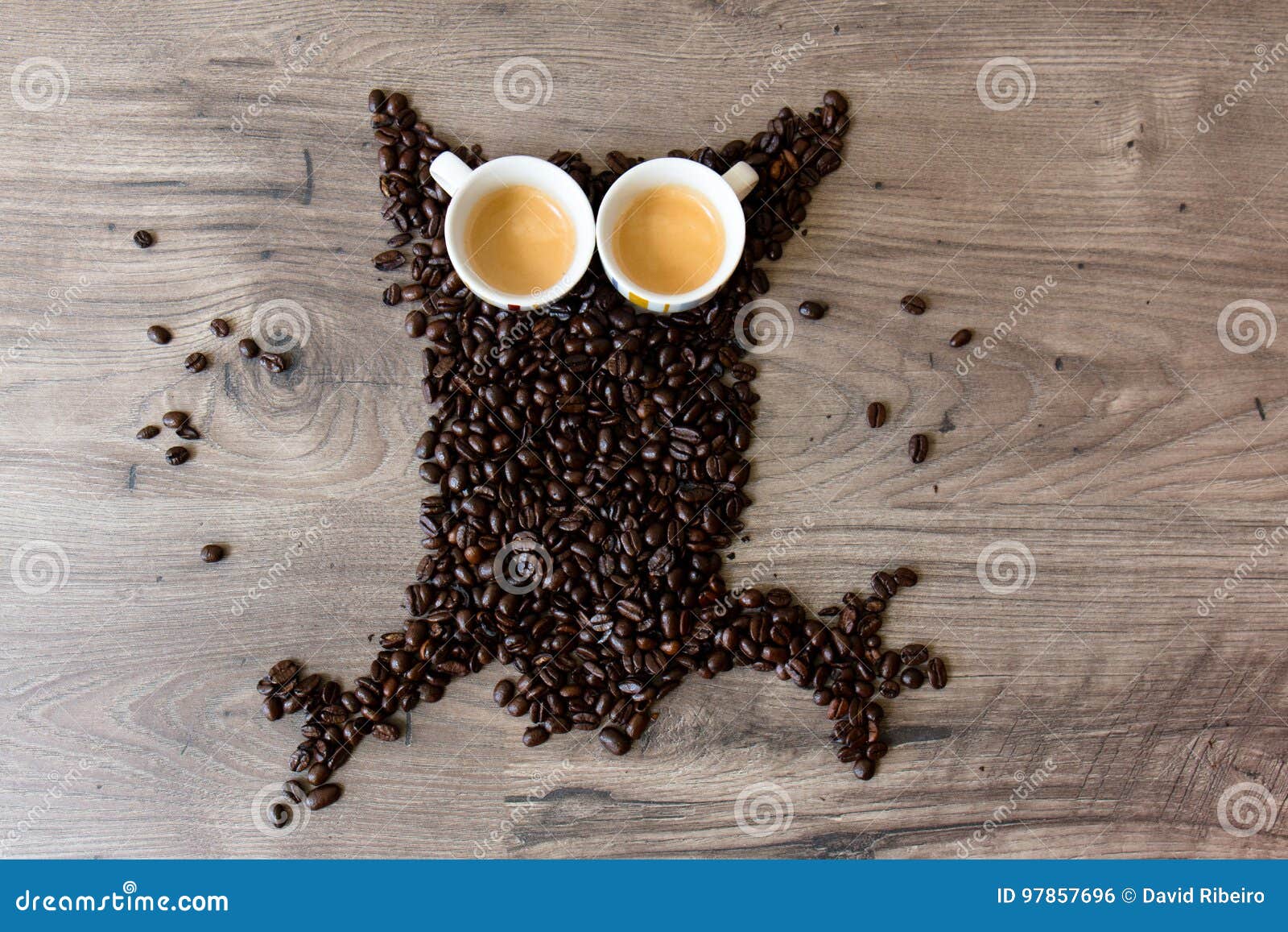A coruja deu forma à figura feita fora dos feijões de café e de dois copos completos do café sobre uma tabela. A coruja deu forma à figura feita fora dos feijões de café e de dois copos vazios do café sobre uma tabela de madeira