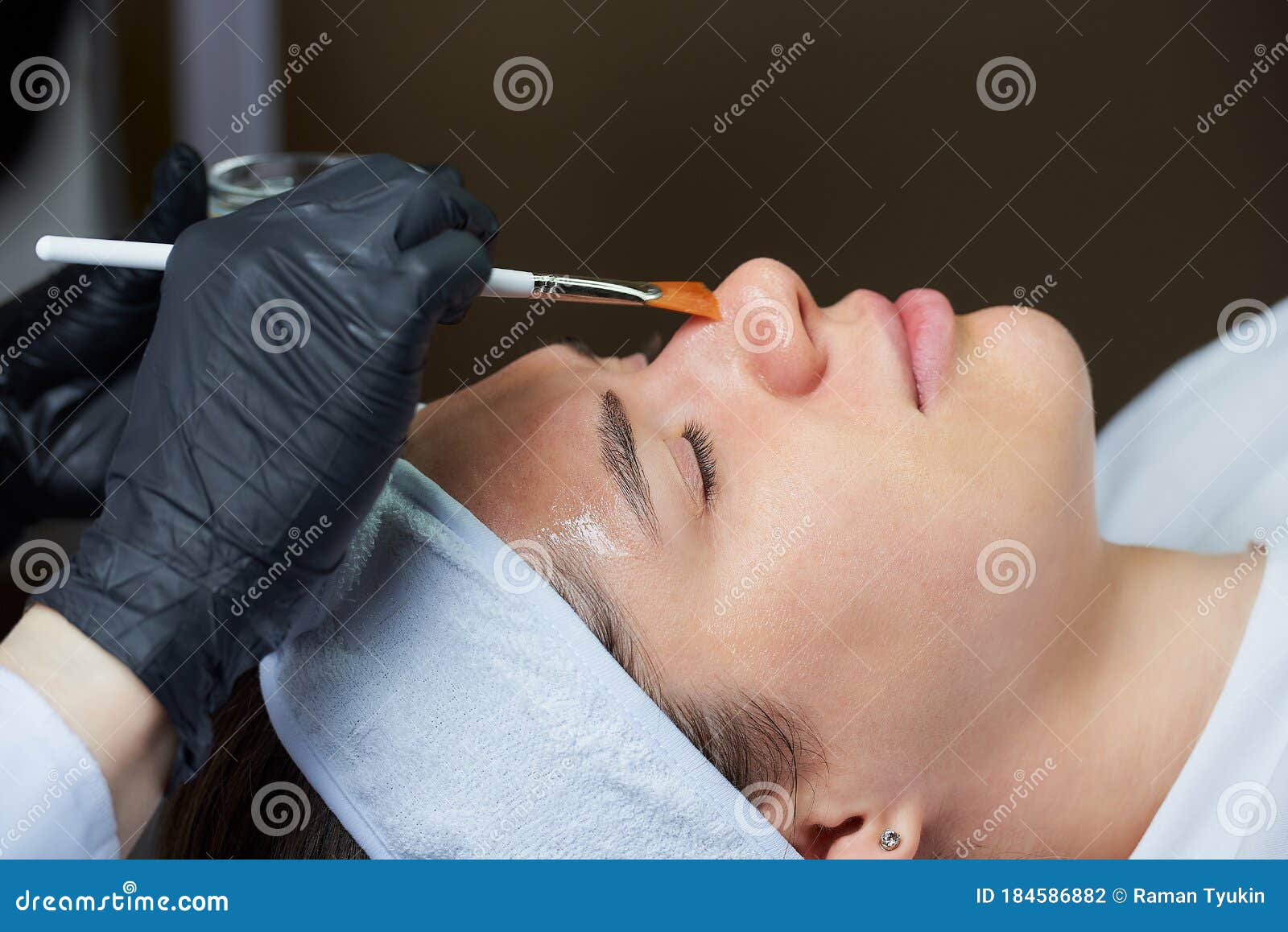 cosmetologist uses a brush to apply a superficial face peeling to a woman