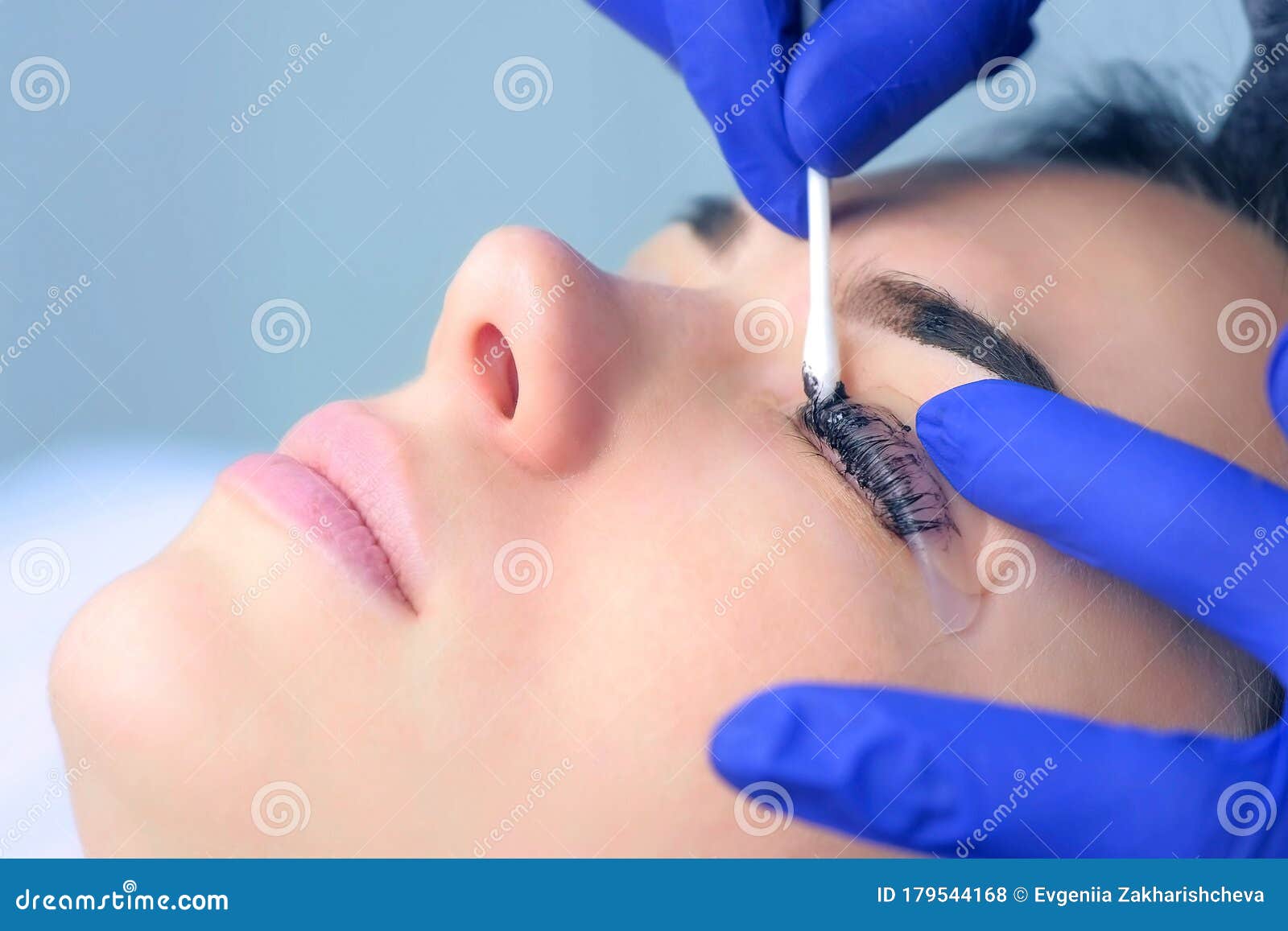 cosmetologist wiping paint from lashes and eyebrows of woman, side view.