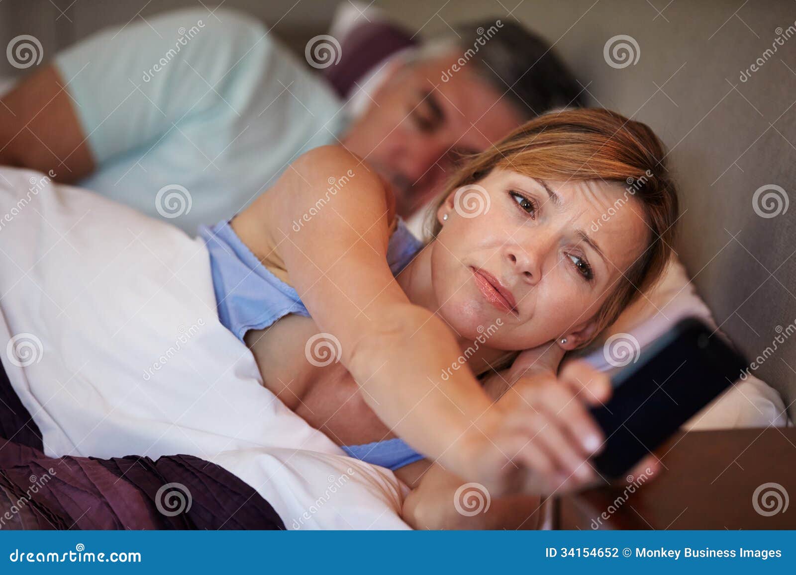 Couple In Bed With Wife Suffering From Insomnia Looking At Mobile Phone