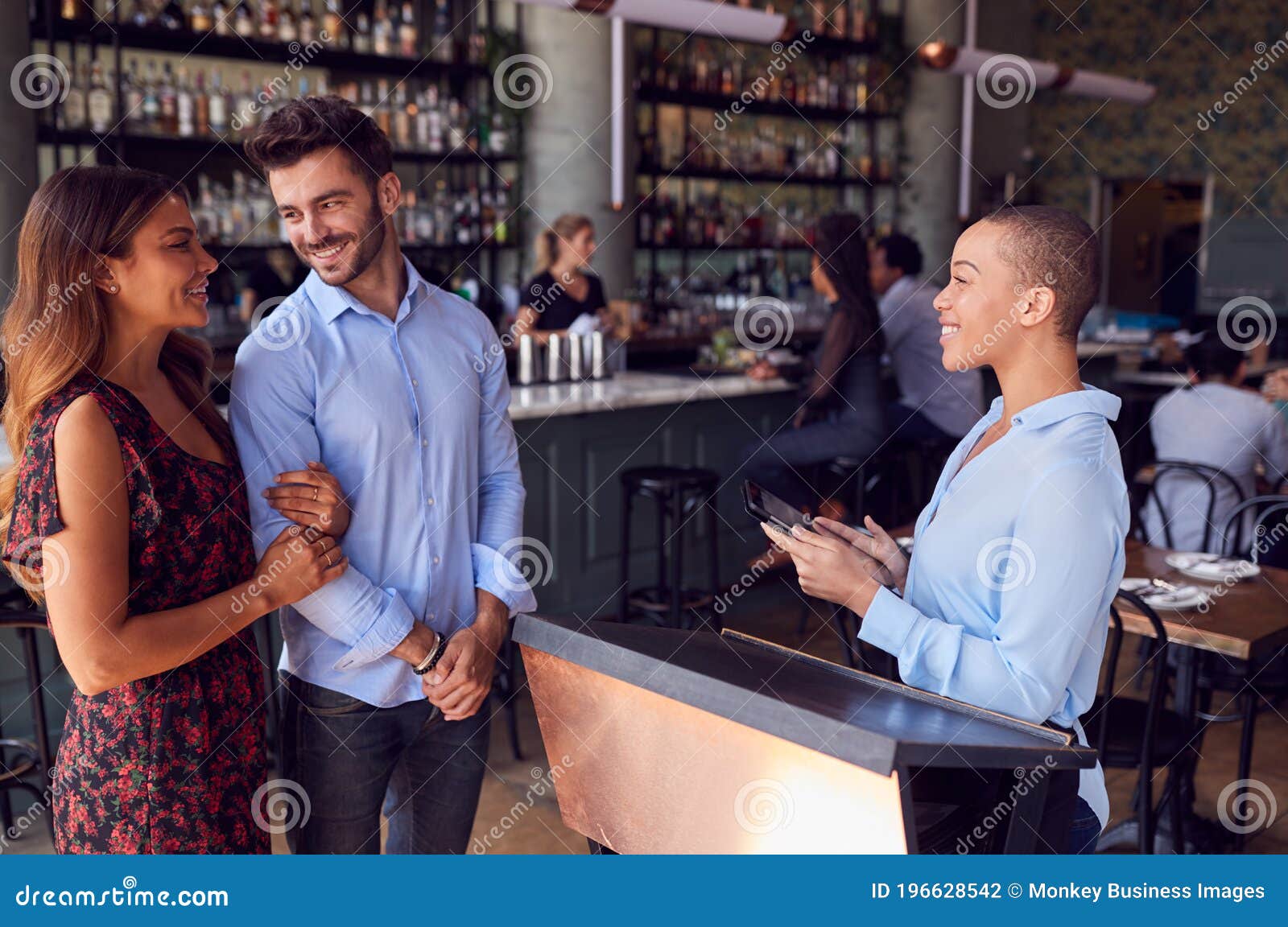 couple being greeted by maitre d using digital tablet as they arrive at restaurant