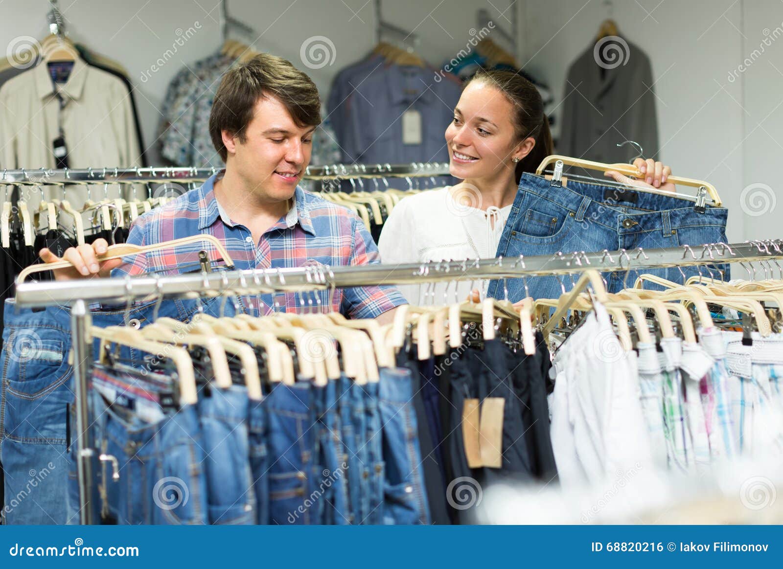 Couple buying blue jeans at store. Smiling young male and female buying blue jeans at store