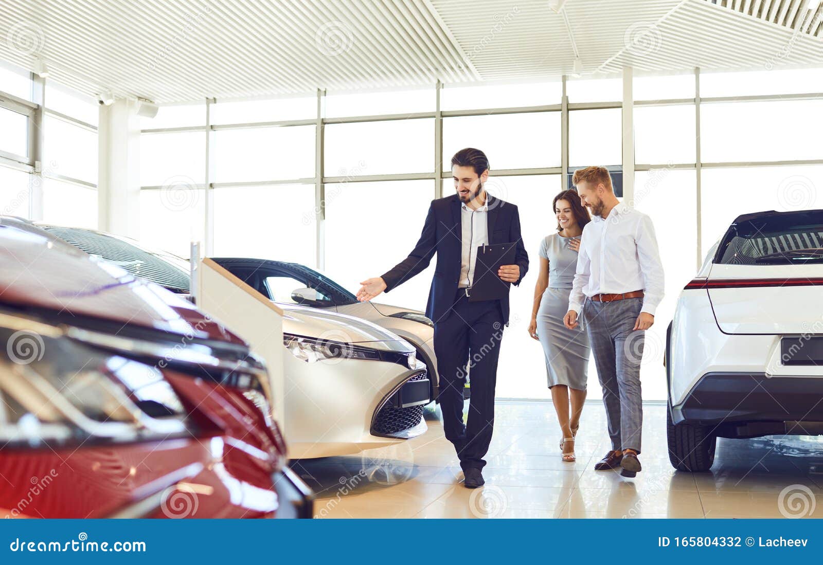 couple and the dealer selling cars look the car in the showroom.