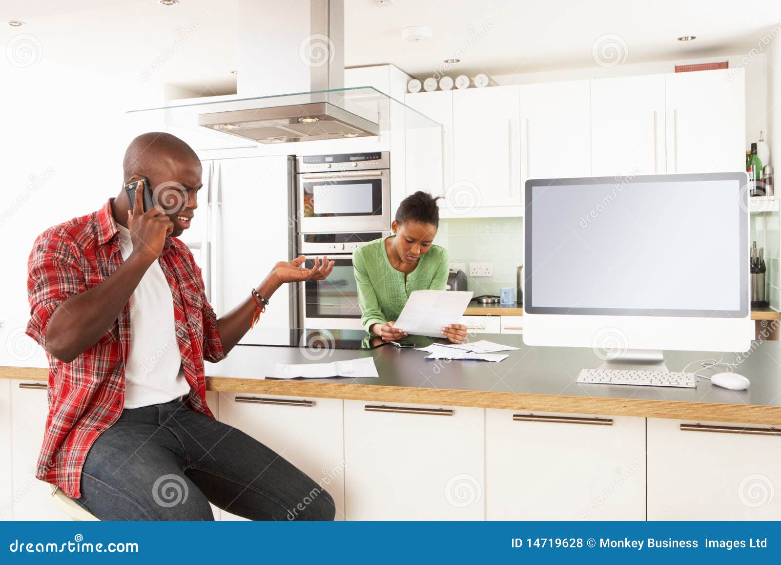  A couple is sitting in their kitchen discussing finances, the man is on the phone and the woman is looking at bills.