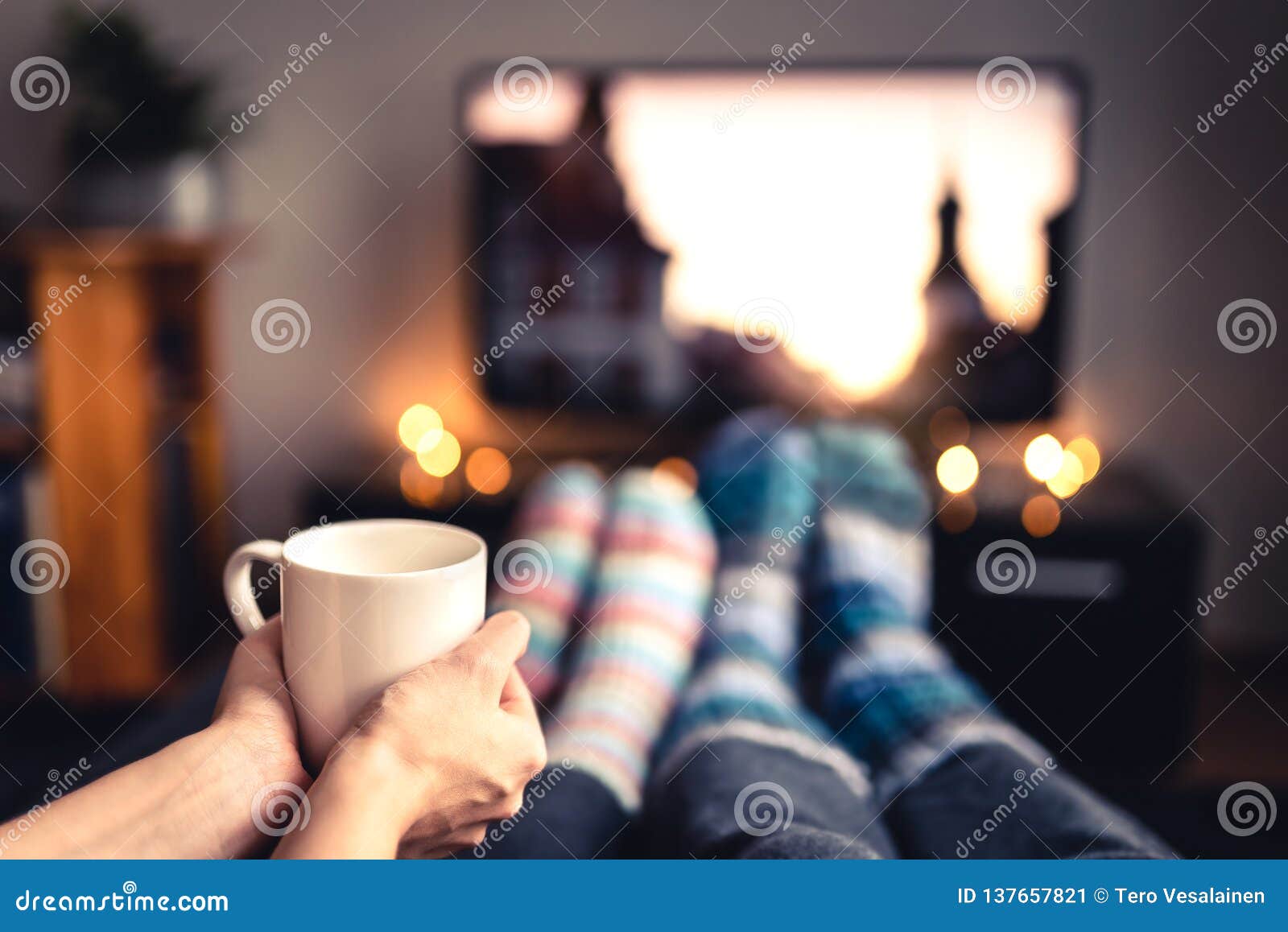 couple drinking tea, hot chocolate, eggnog or mulled wine and watching tv in warm cozy woolen socks in winter.