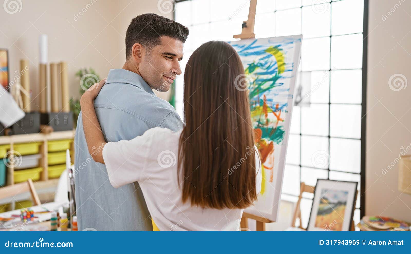 couple embracing in art studio with colorful paintings and large windows showcasing creativity and partnership