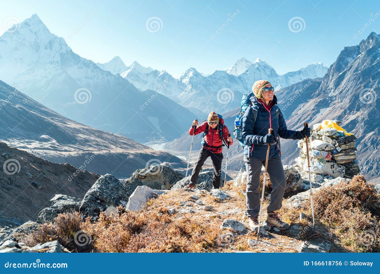 couple following everest base camp trekking route near dughla 4620m. backpackers carrying backpacks and using trekking poles and