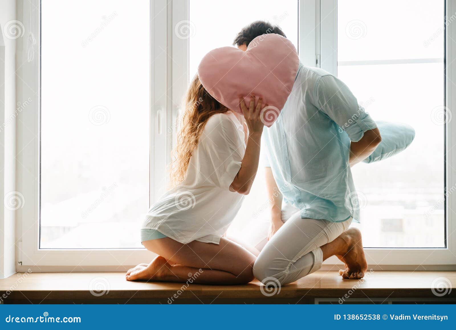 couple girl and guy play with pillows near window.