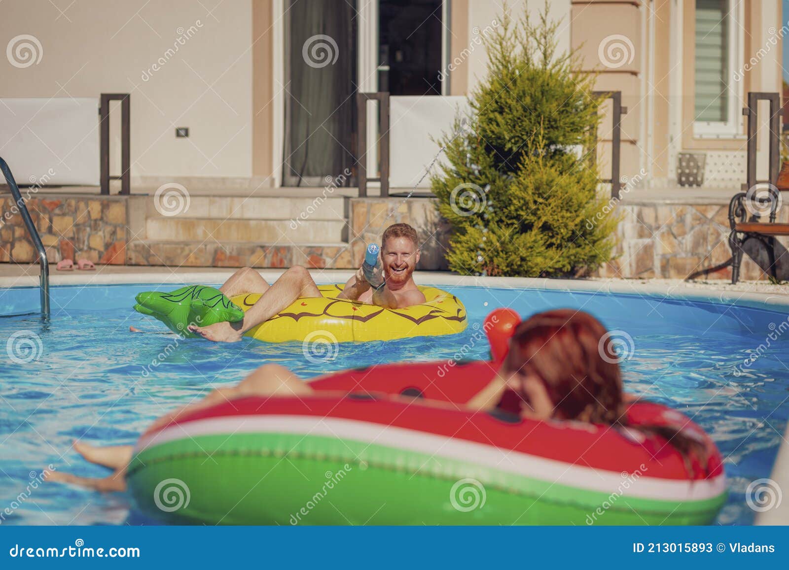 Couple Having Fun Splashing Water On Each Other At The Swimming Pool