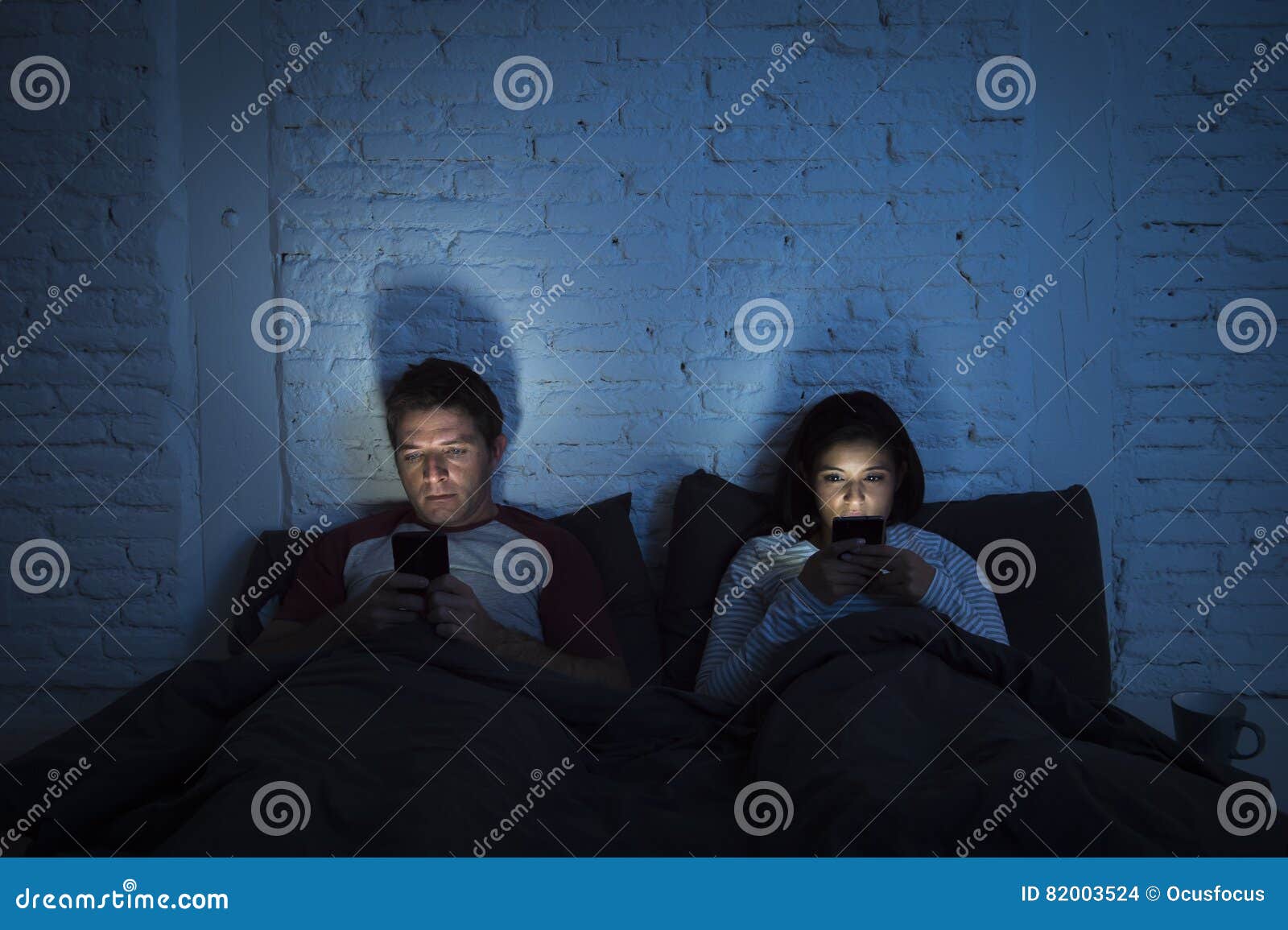 couple at home in bed late at night using mobile phone in relationship communication problem