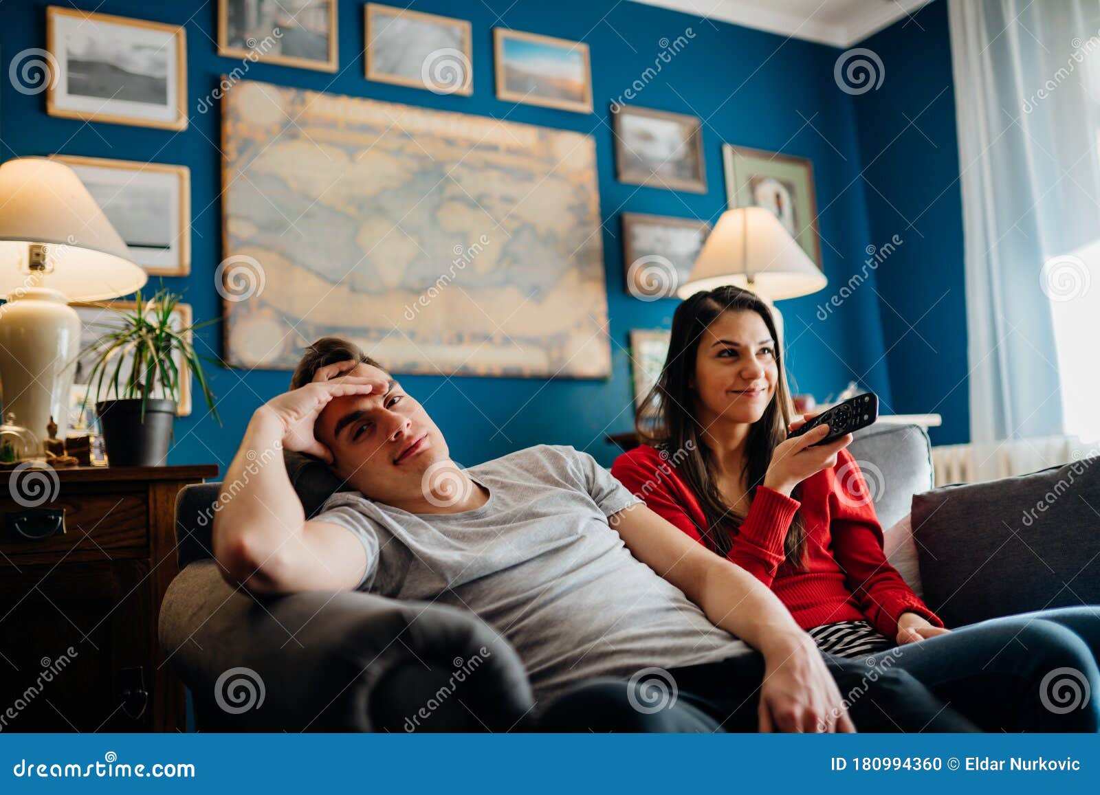 couple at home watching tv.remote control fight won by girlfriend.boyfriend bored by tv program.watching her favorite show/film.