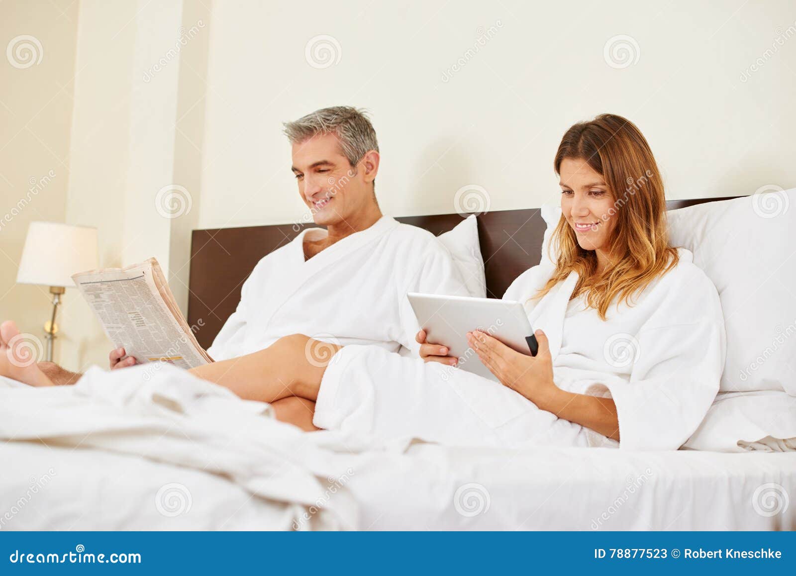 Couple in Hotel Room Reading Newspaper and Tablet Computer Stock Image