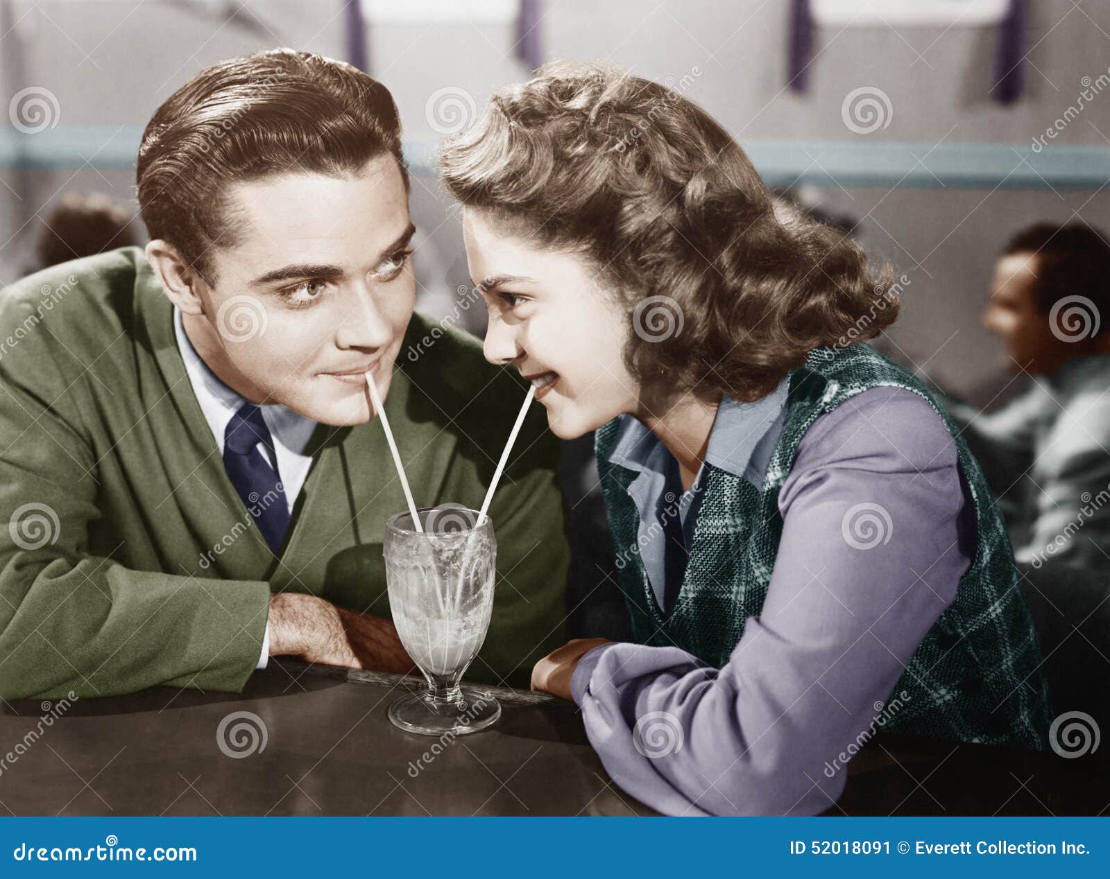 couple in a restaurant looking at each other and sharing a milk shake with two straws