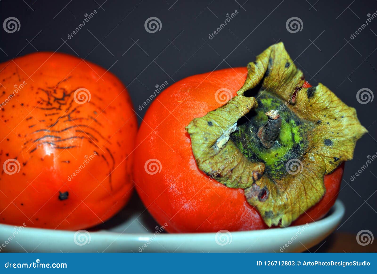couple of ripe persimons macro detail in white plate on dark background