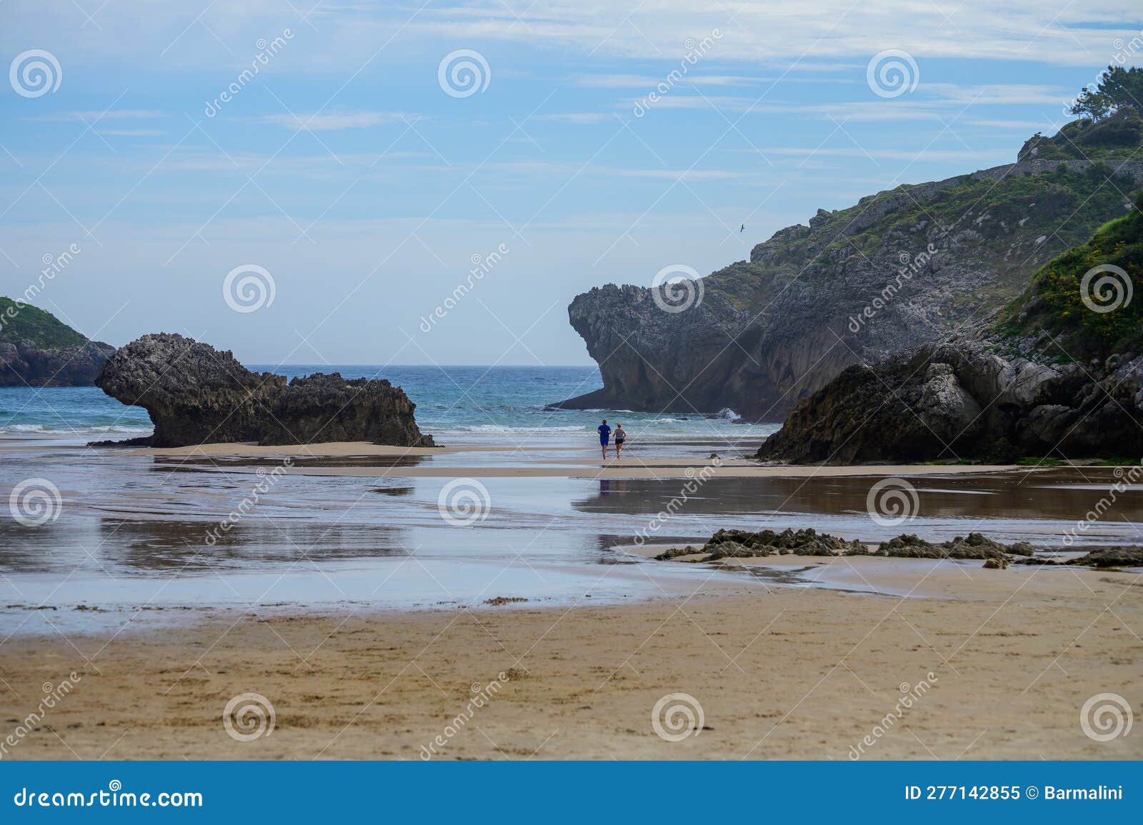 couple running on playa de palombina las camaras in celorio, green coast of asturias, north spain with sandy beaches, cliffs,
