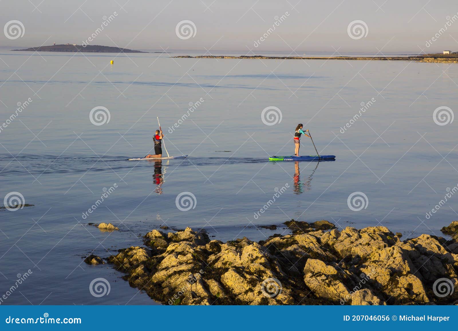 A Couple Slowly Paddle Their Surf Boards In The Calm Sea At Groomsport
