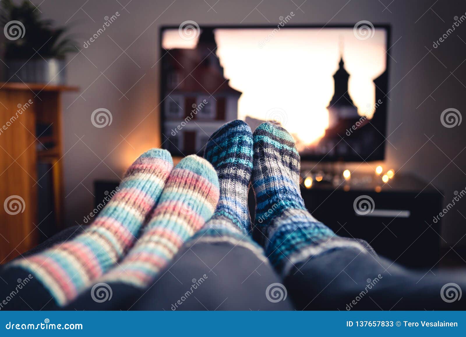 couple with socks and woolen stockings watching movies or series on tv in winter. woman and man sitting or lying together on sofa.